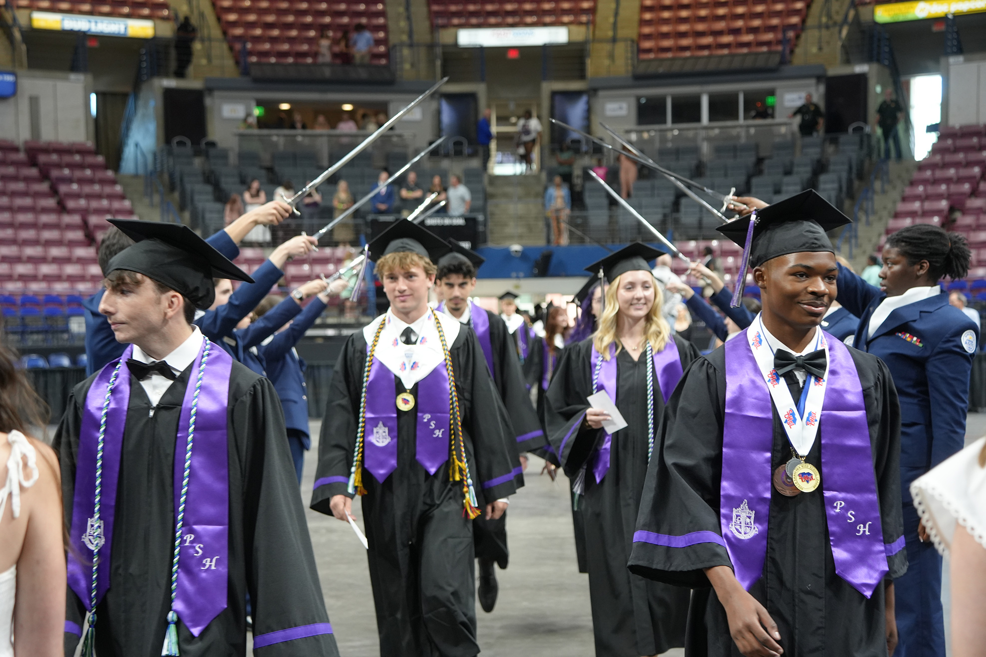 A group of people in graduation gowns and hats are walking in a line at an event.