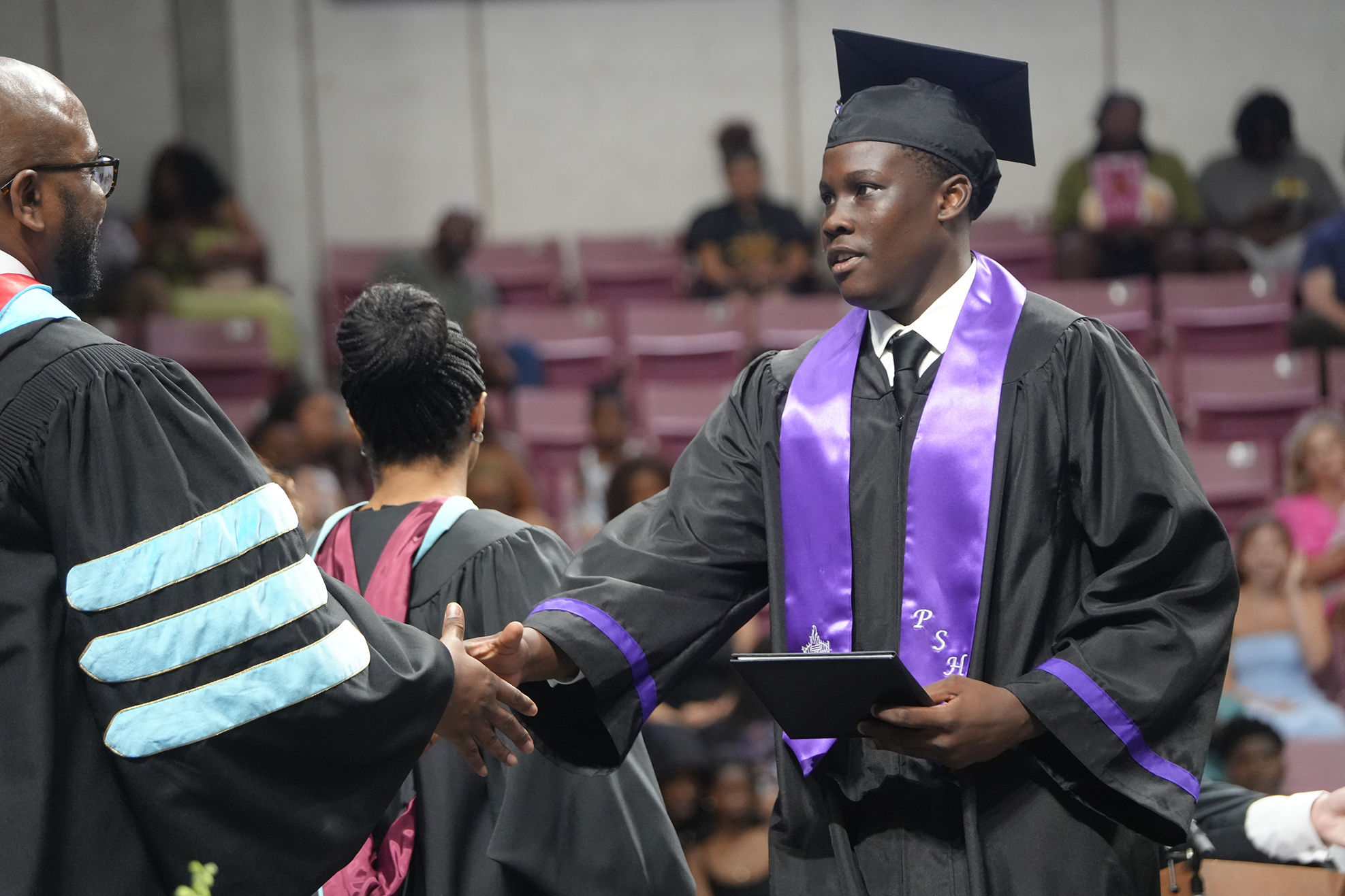 A man in a graduation gown shakes hands with a faculty member during a ceremony.