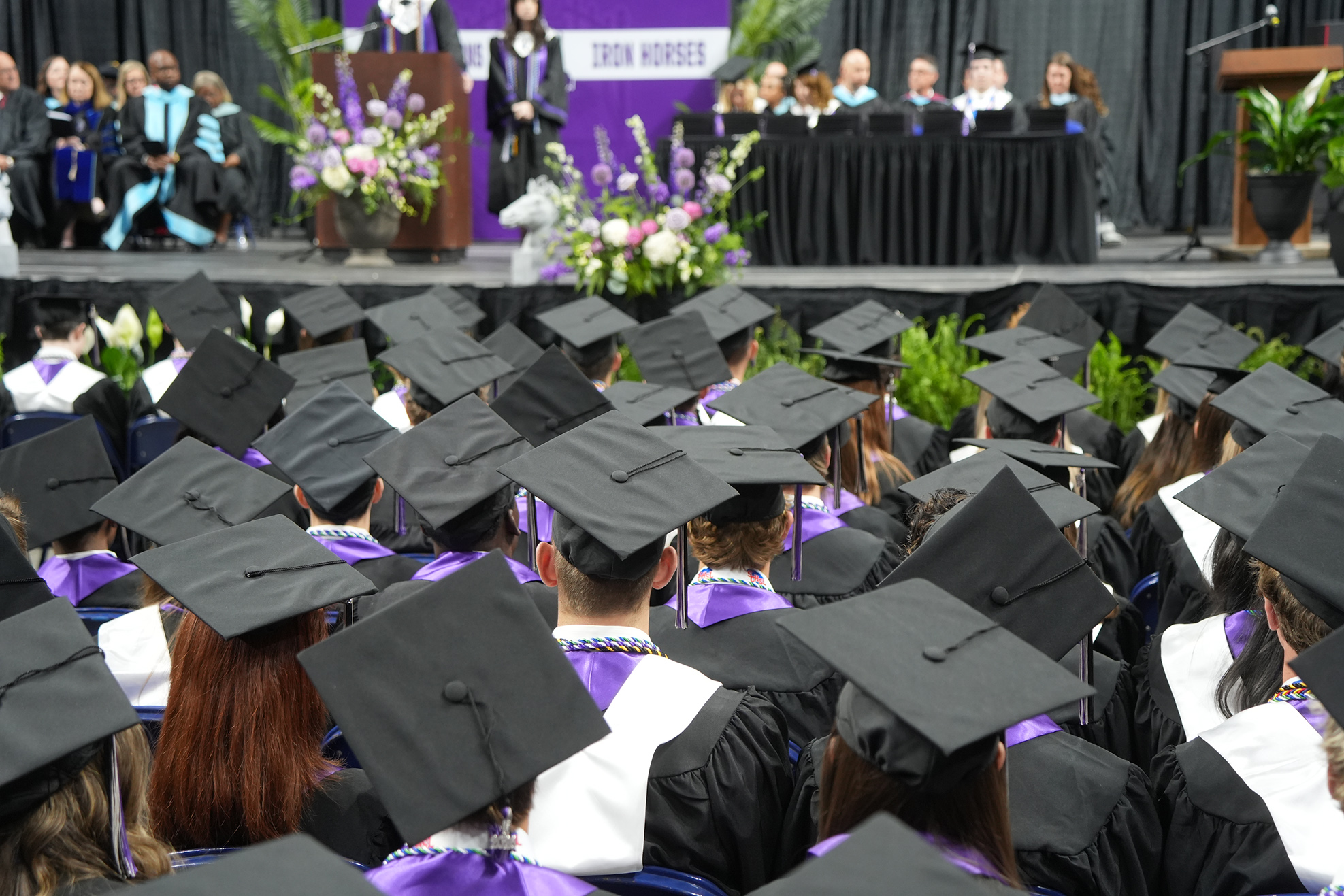 A large group of people wearing graduation gowns and caps sit in a theater during an event.