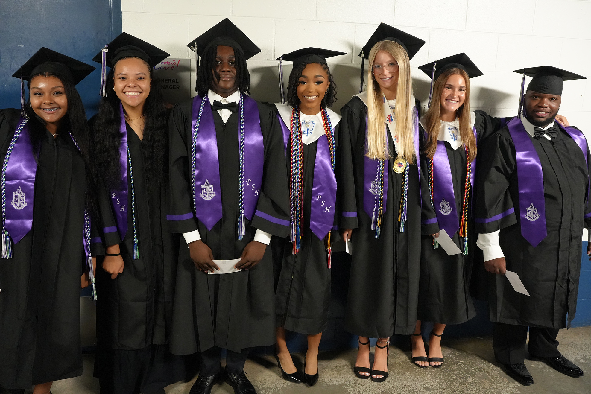 A group of six individuals in graduation attire, including gowns and caps, pose for a photo.