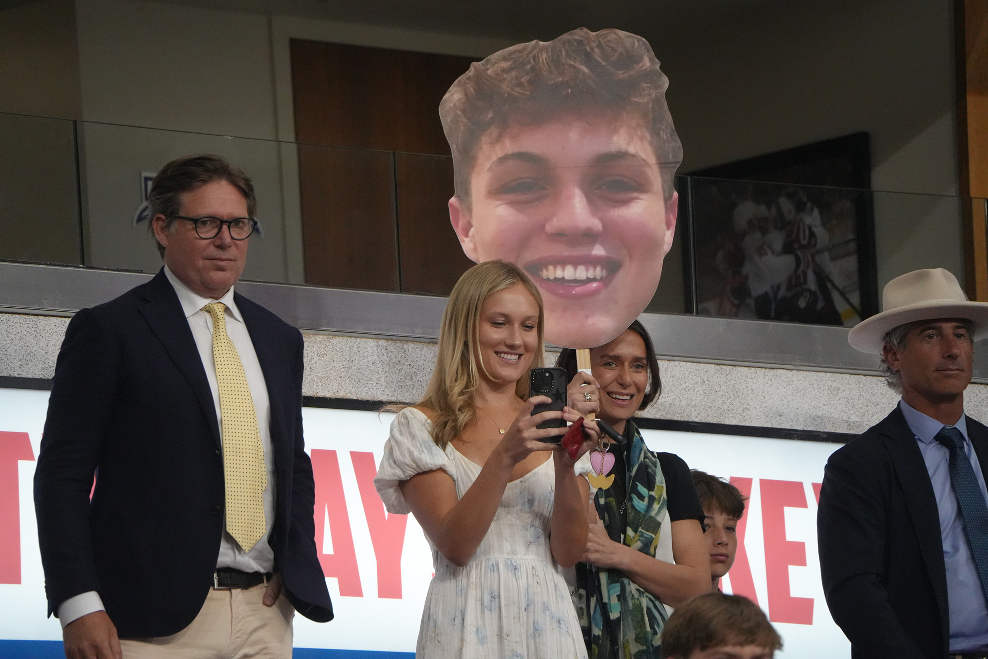 Group of people at an event with a large head cutout on a stand behind them.