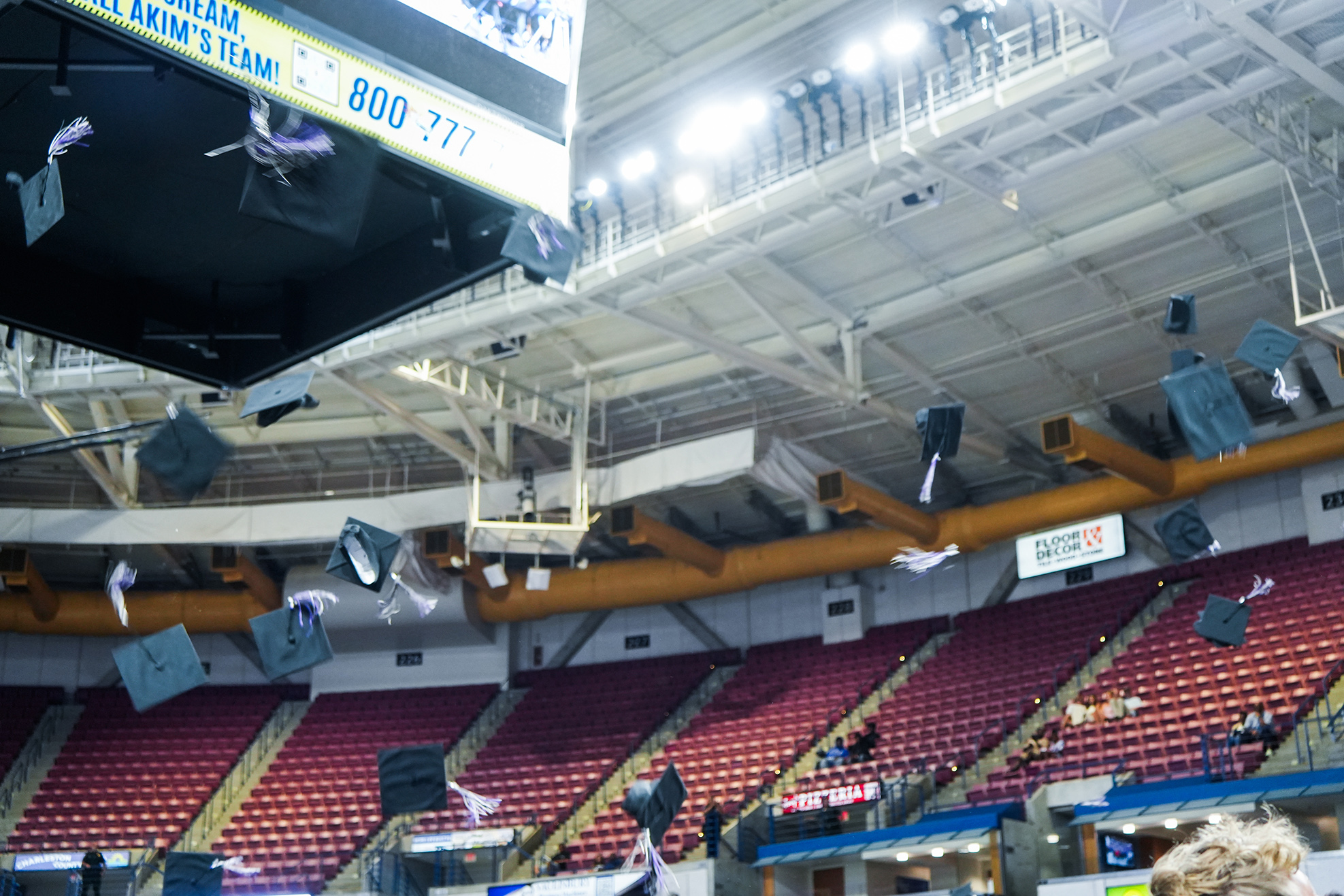 An indoor arena with red seats and a large digital scoreboard. Confetti and caps fall from the ceiling.