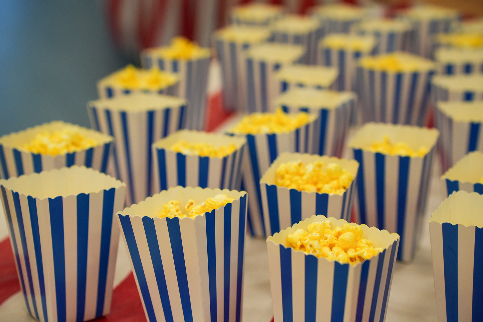 A table with popcorn in striped paper cups. The popcorn is golden and the stripes are blue and white.
