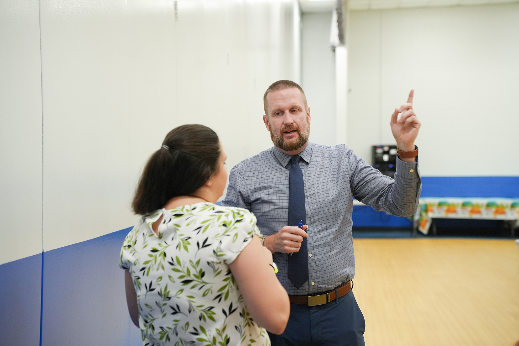 A man and a woman are standing, with the man gesturing towards something and the woman looking at him.