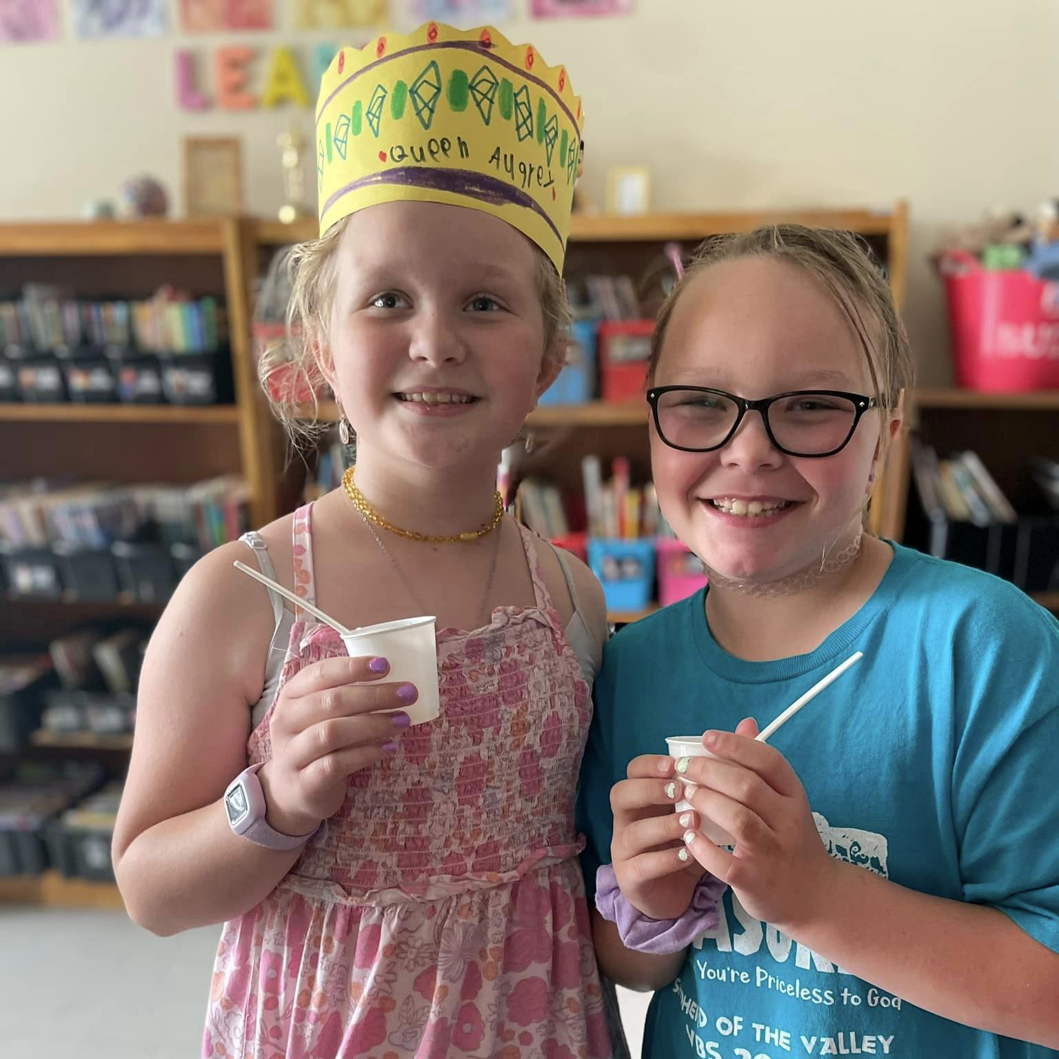 Two students smiling at the camera, one's wearing a paper crown