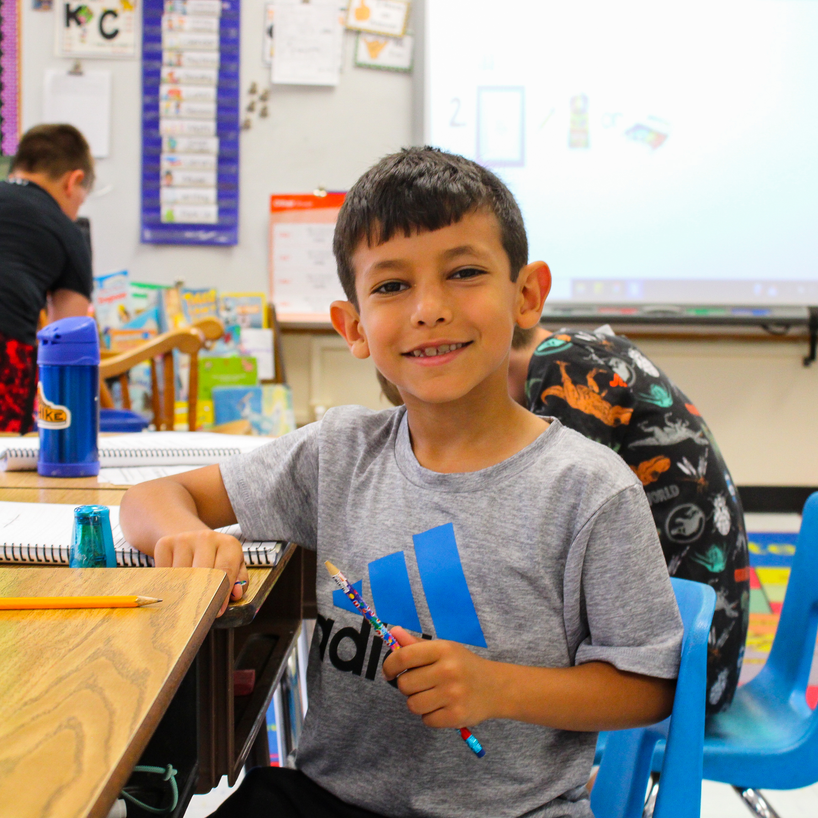 A student sitting at his desk, smiling at the camera