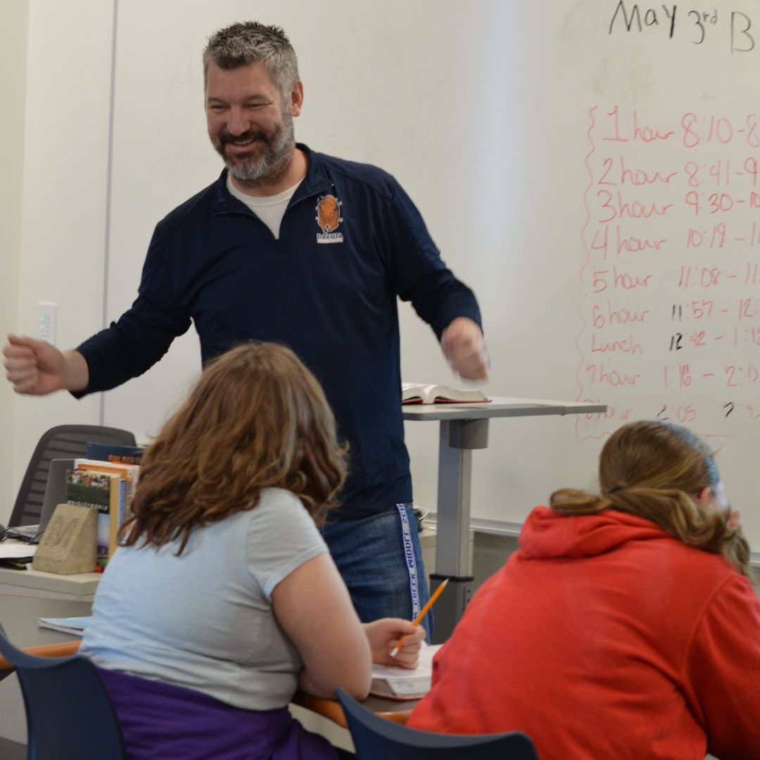 Interactive Dakota teacher giving students a lesson in class while the students take notes at their desks.