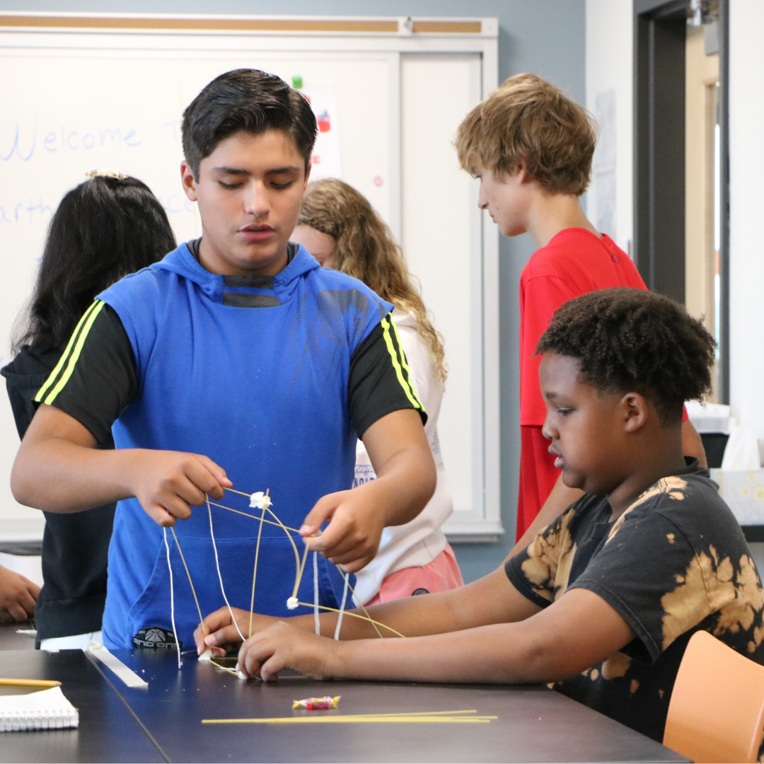 Two male students working on a STEM building exercise with toothpicks and marshmellows at a desk.