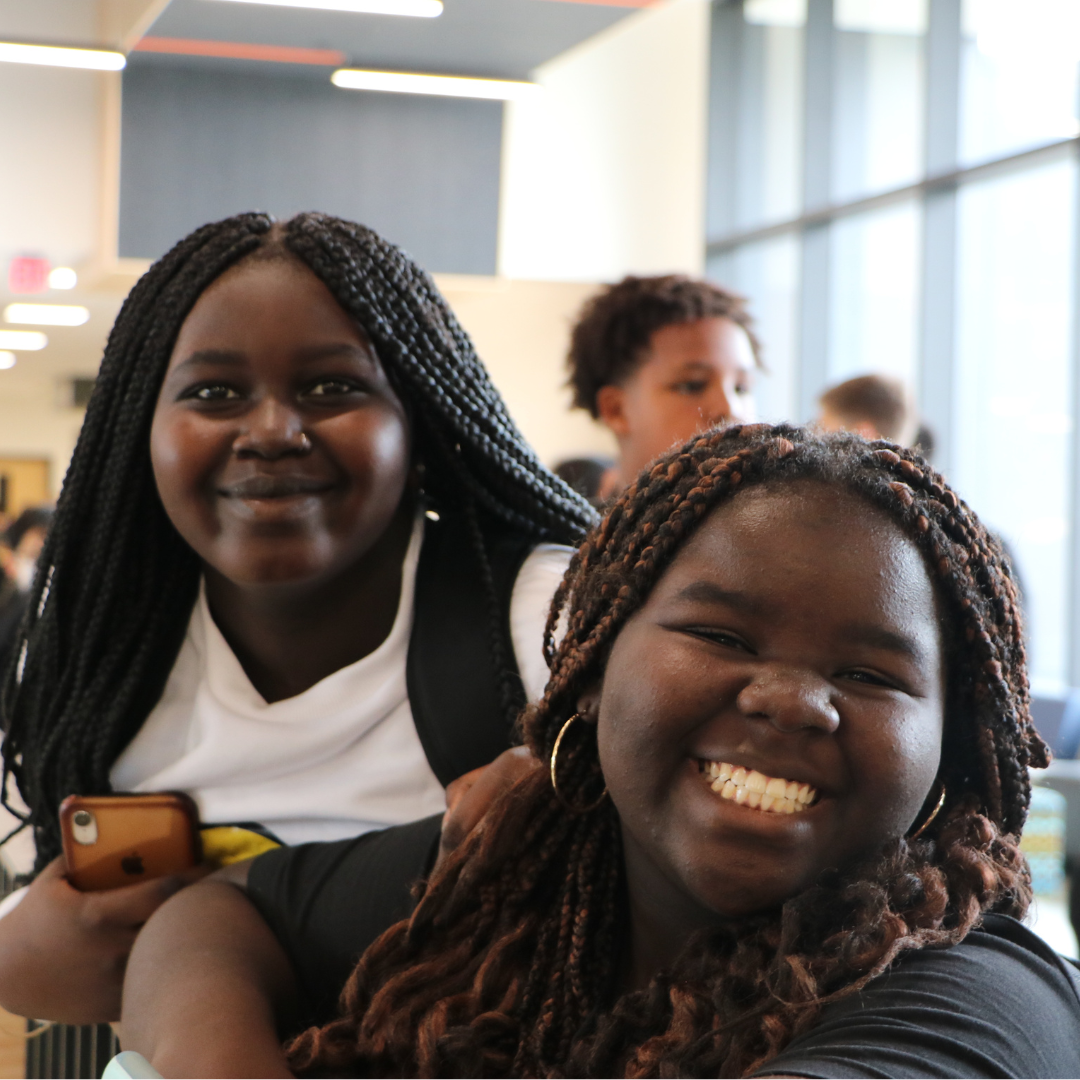 Two female students leaning on the railing of the first floor while smiling at the camera .