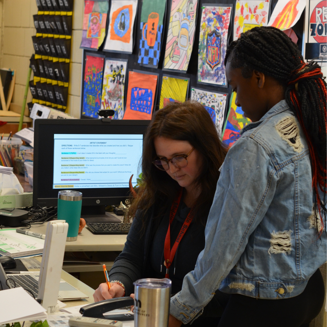 Teacher helping a student at her desk with a question on an assignment.