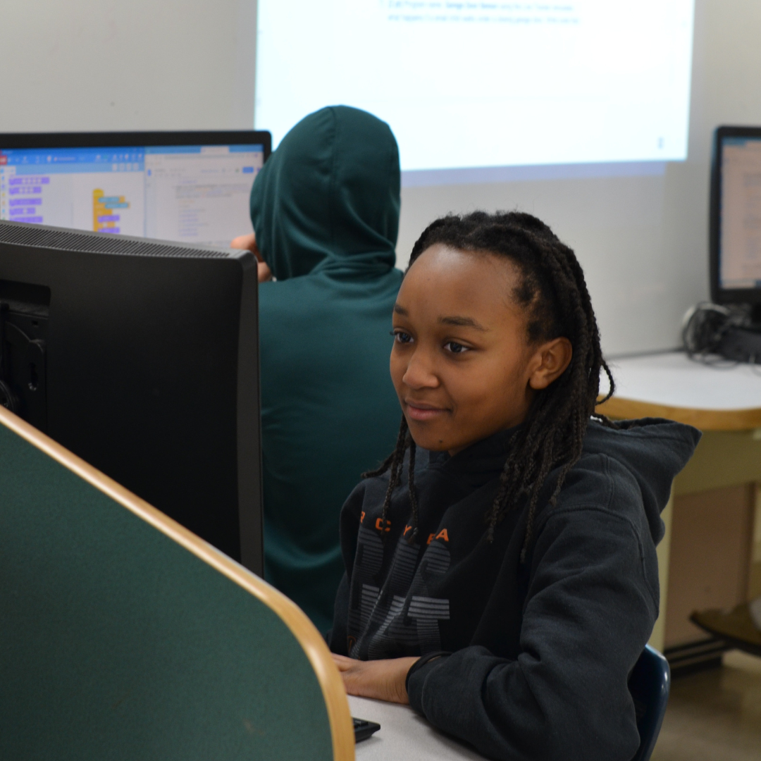 Student wearing a sweatshirt looking at the computer in the JA computer lab