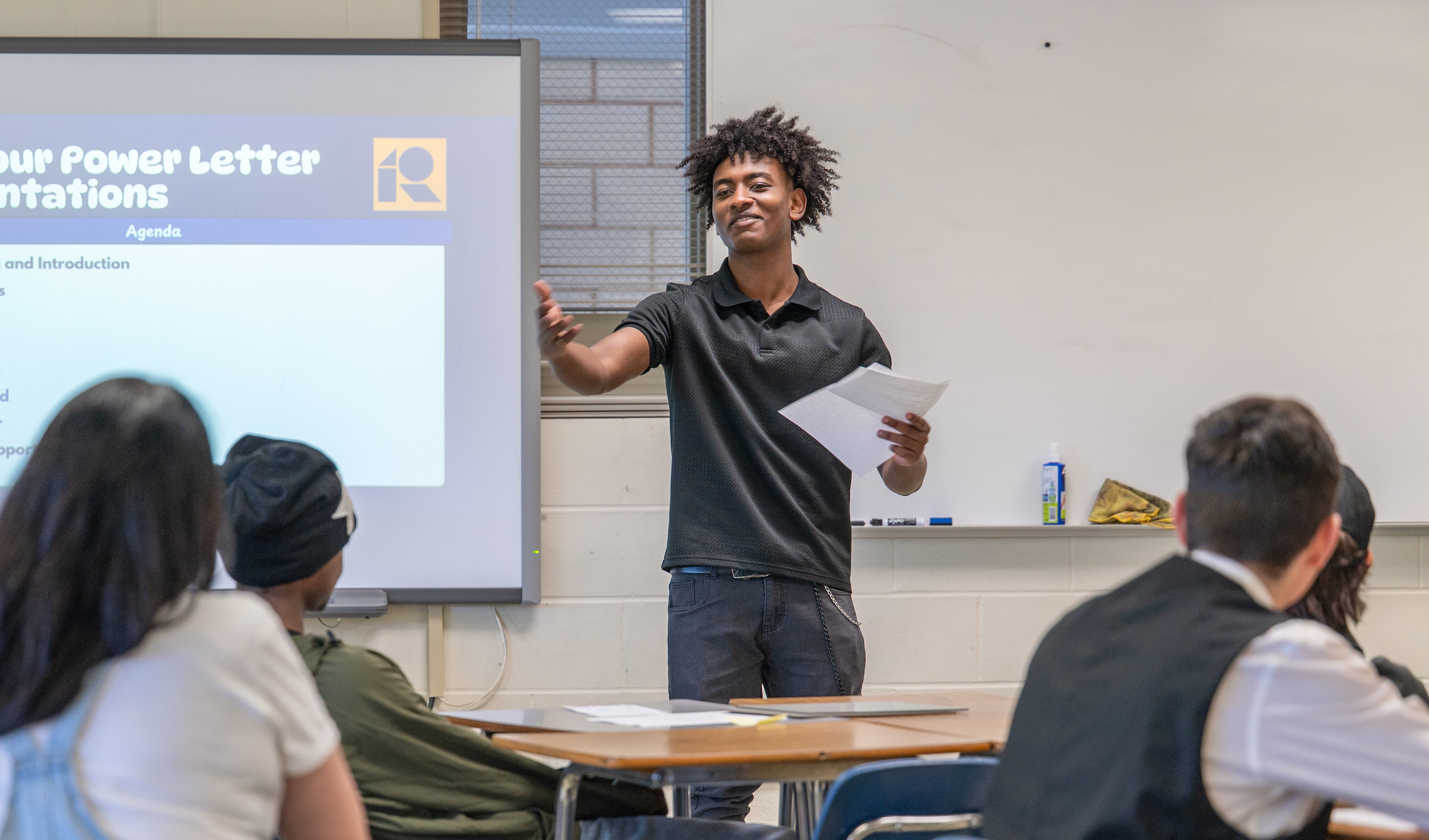High school senior presents in front of his class. The powerpoint on the whiteboard behind him says, "5th Hour Power Letter Presentations."