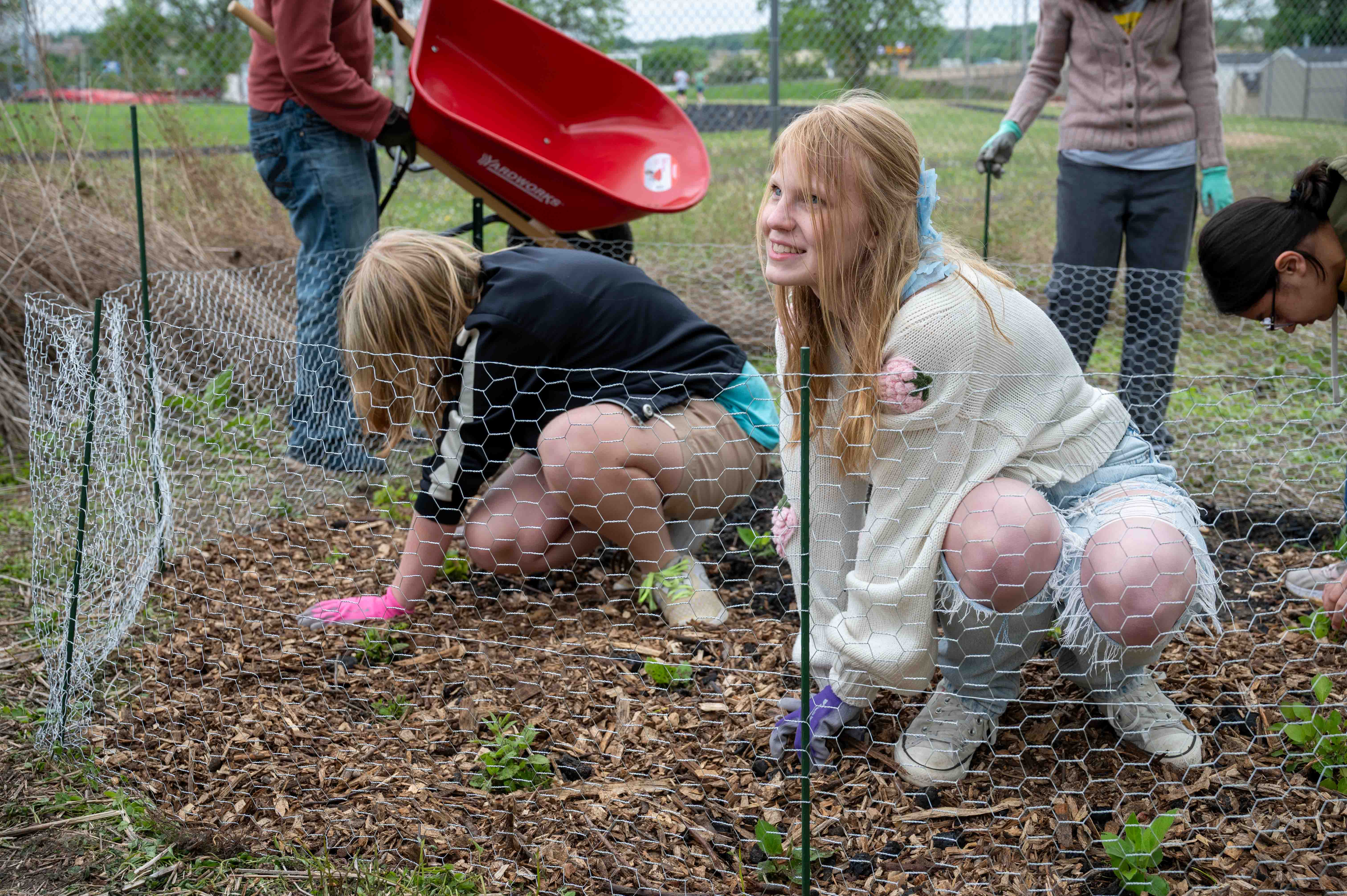 Two students from the gardening club kneel as they spread mulch to help beautify JM's property.