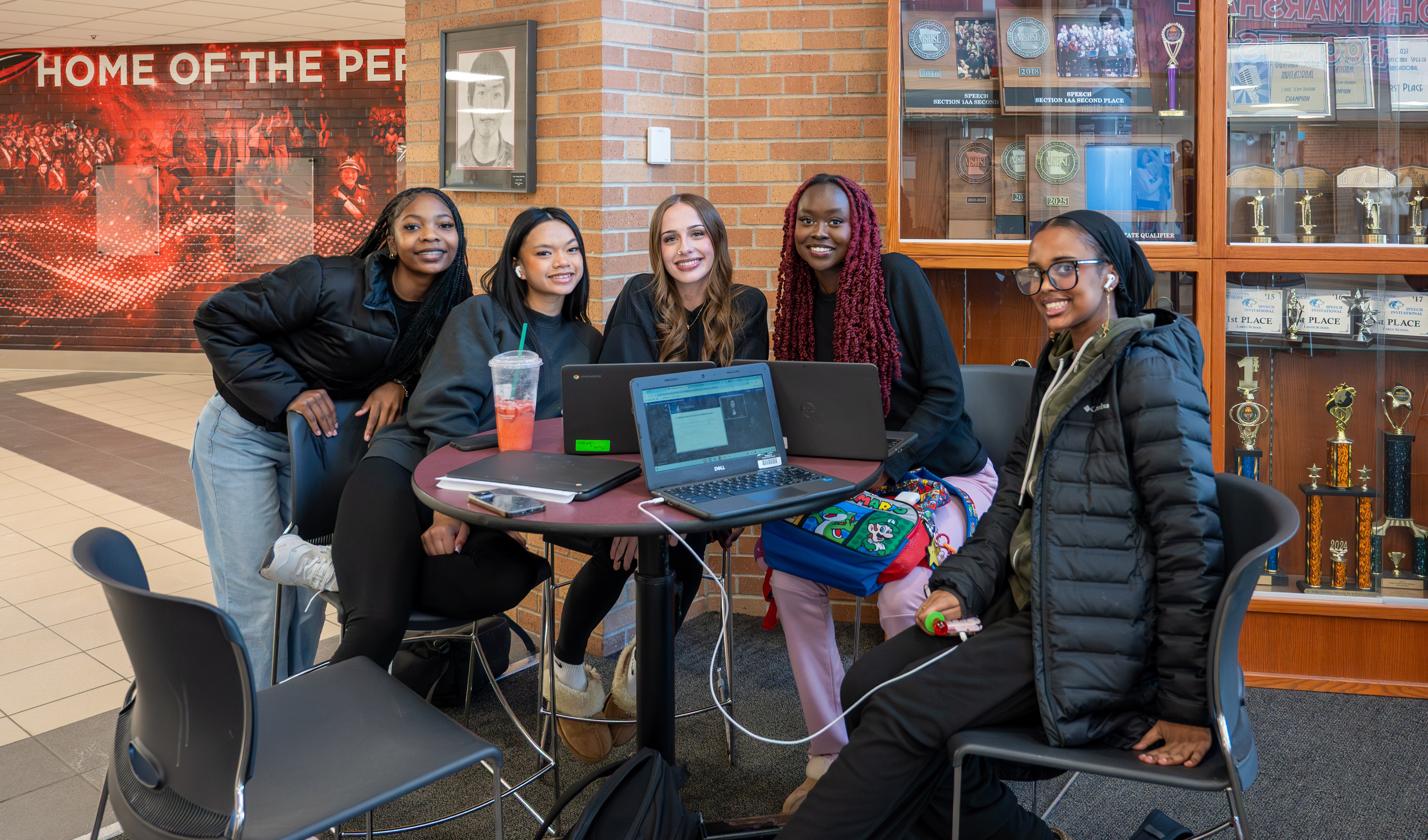 Five students break from studying to smile for a picture in front of a trophy case..