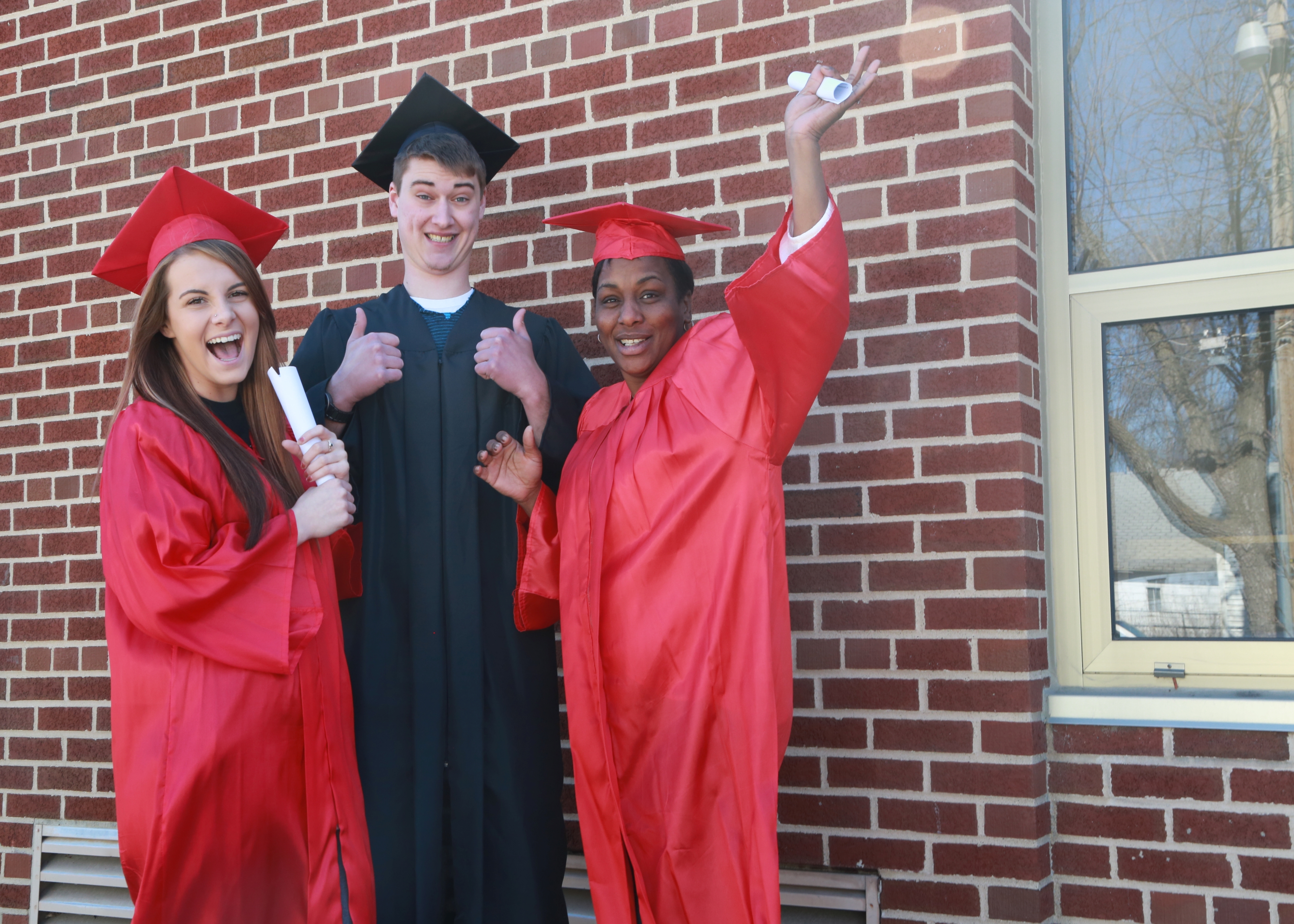 3 college graduates in cap and gown outside a brick building