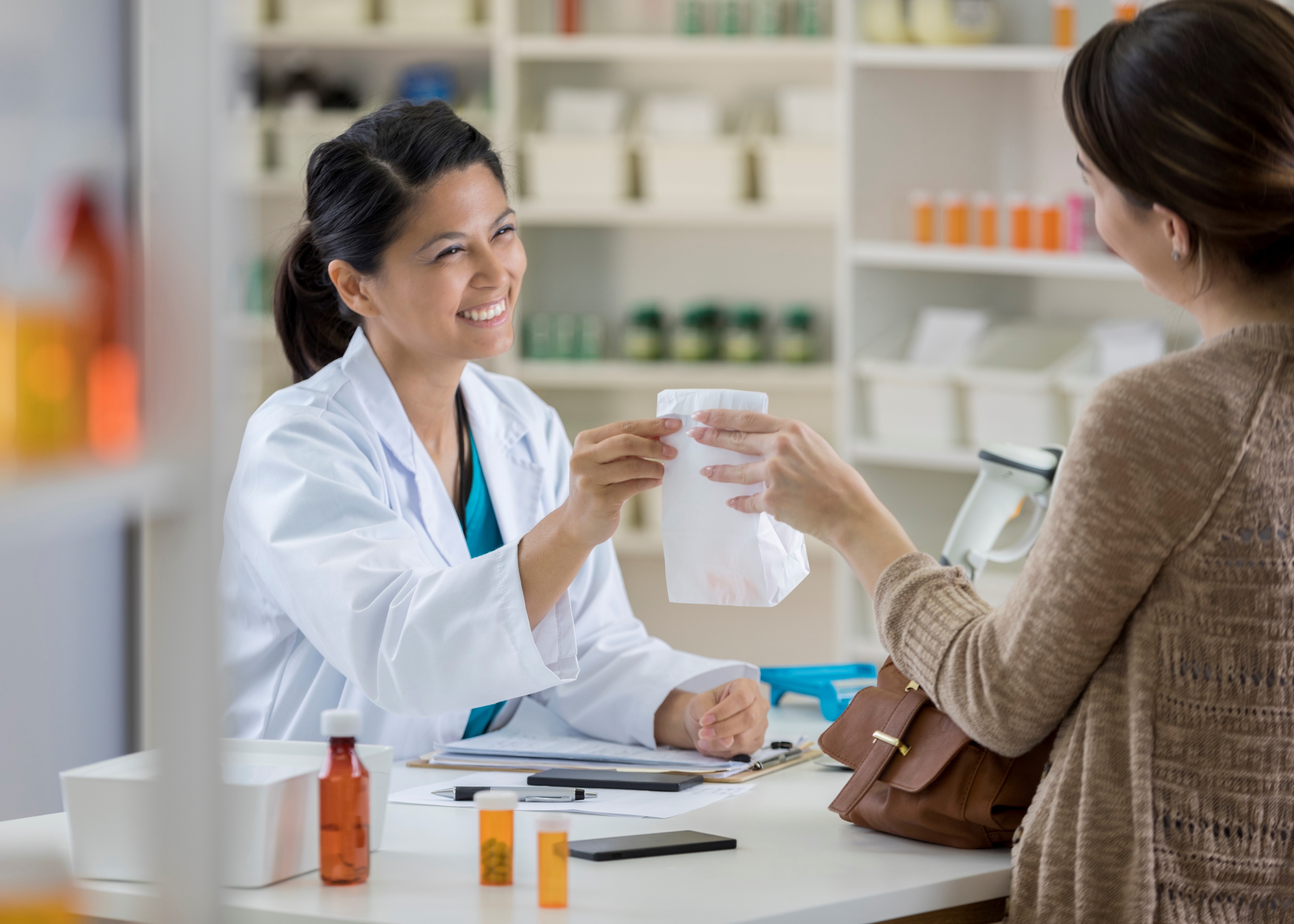 smiling pharmacist handing a paper bag to a customer