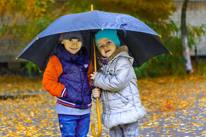 2 young children standing underneath a blue umbrella
