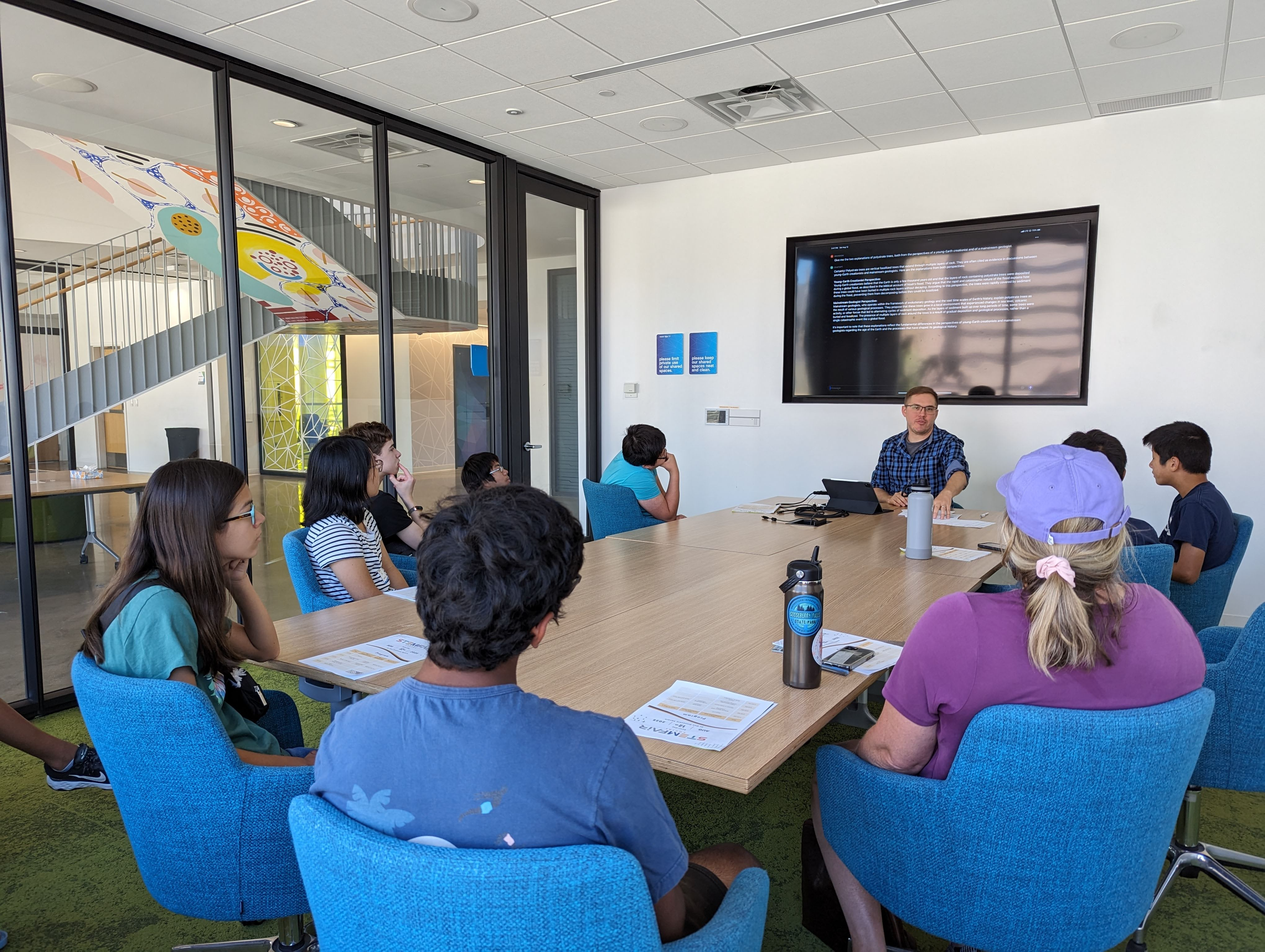 high school students sitting at a conference table, looking at presenter