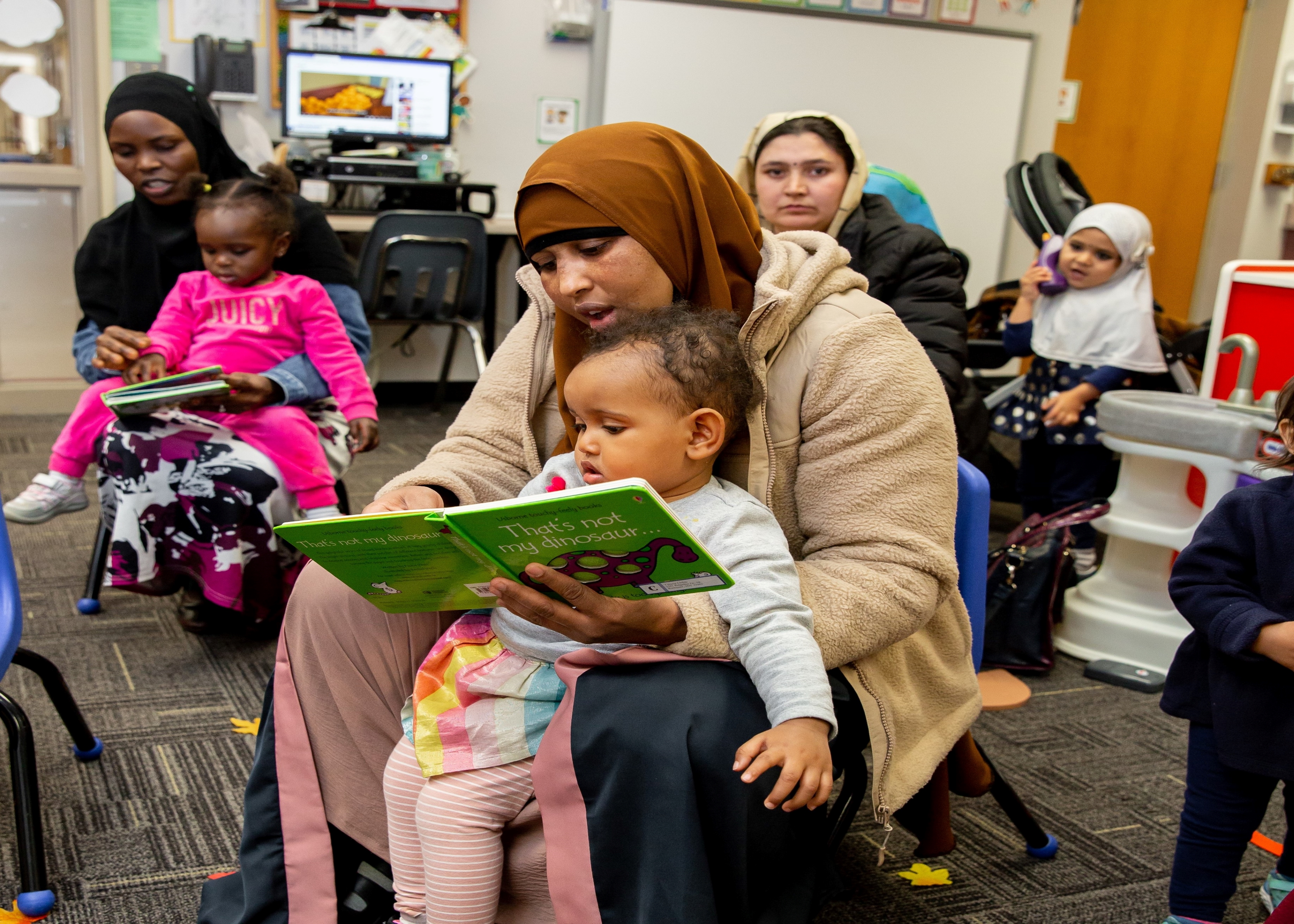 young mother holding her toddler reading a book in a classroom