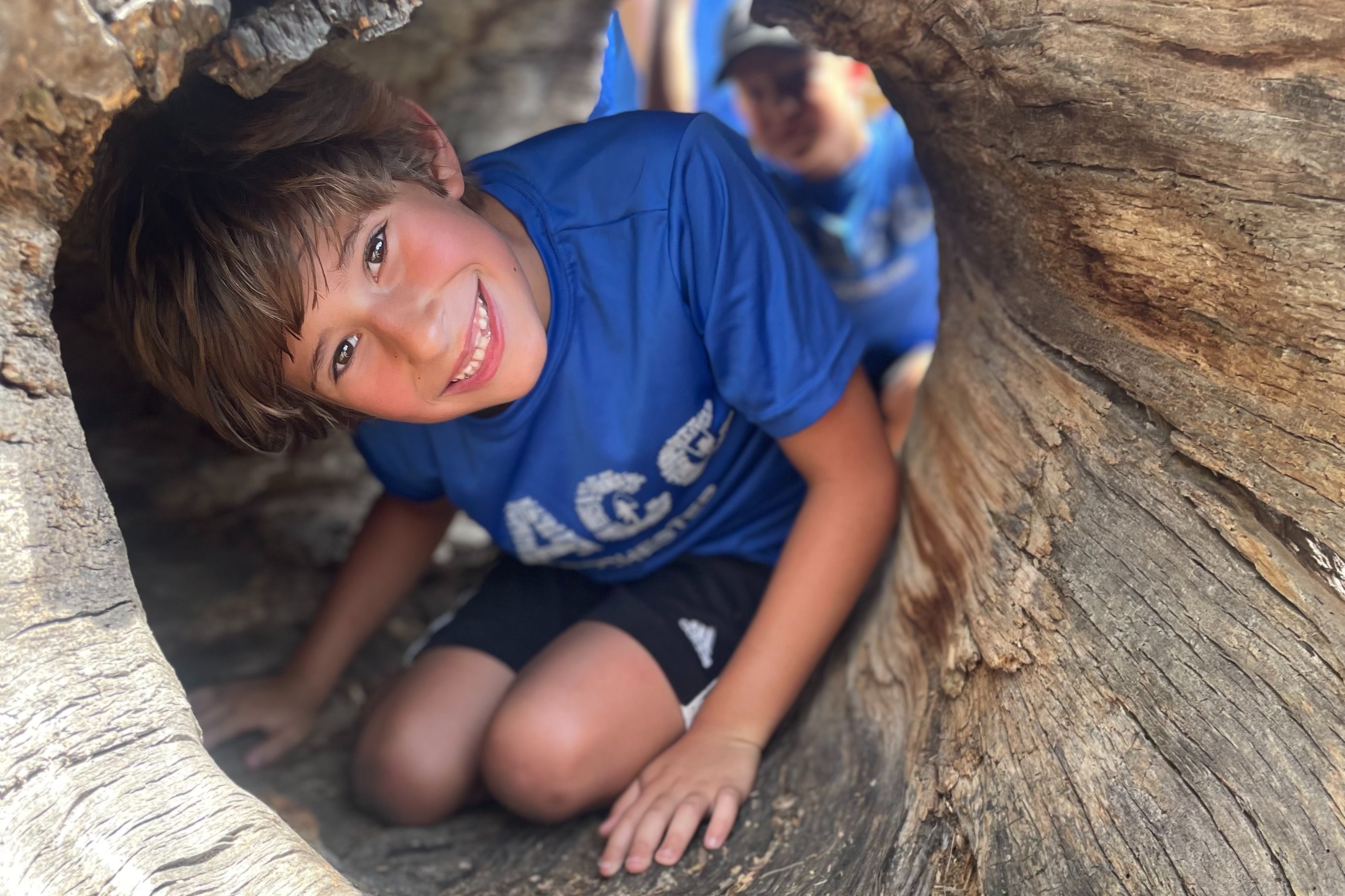 boy in SACC t-shirt posing in hollowed out log