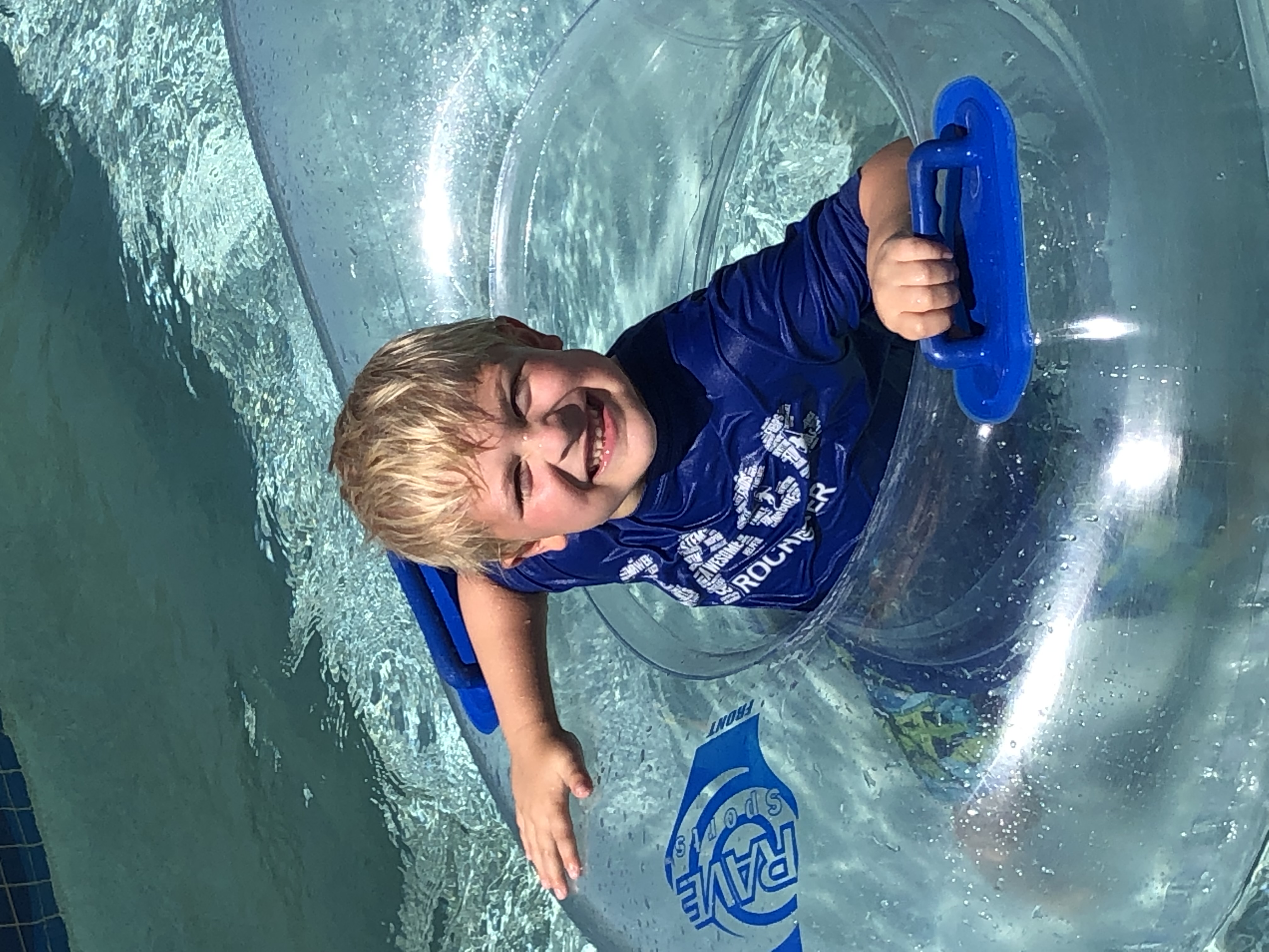 boy smiling in SACC t-shirt in innertube in pool