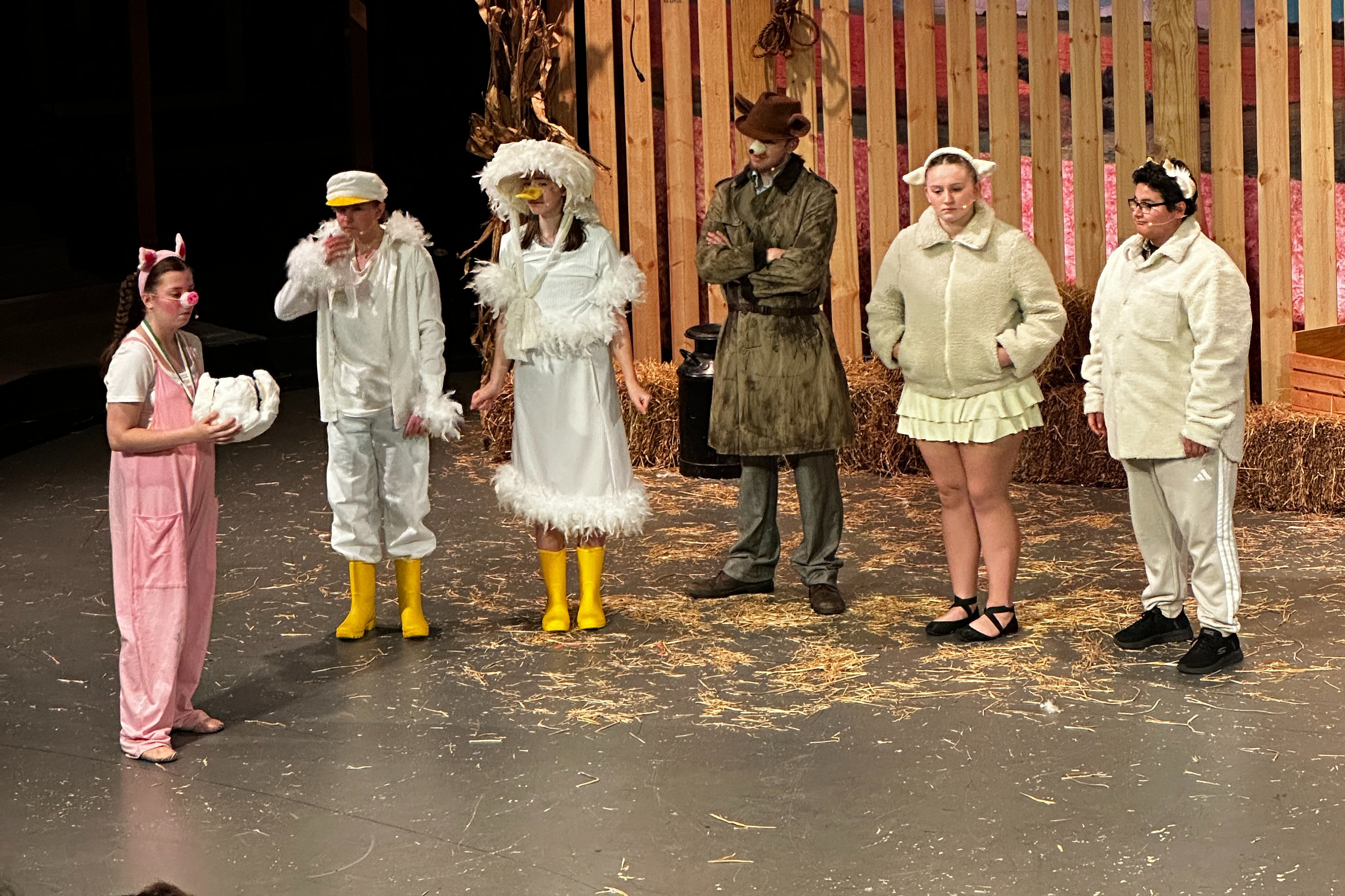 Six people stand on a stage in front of a barn set, wearing costumes and boots.
