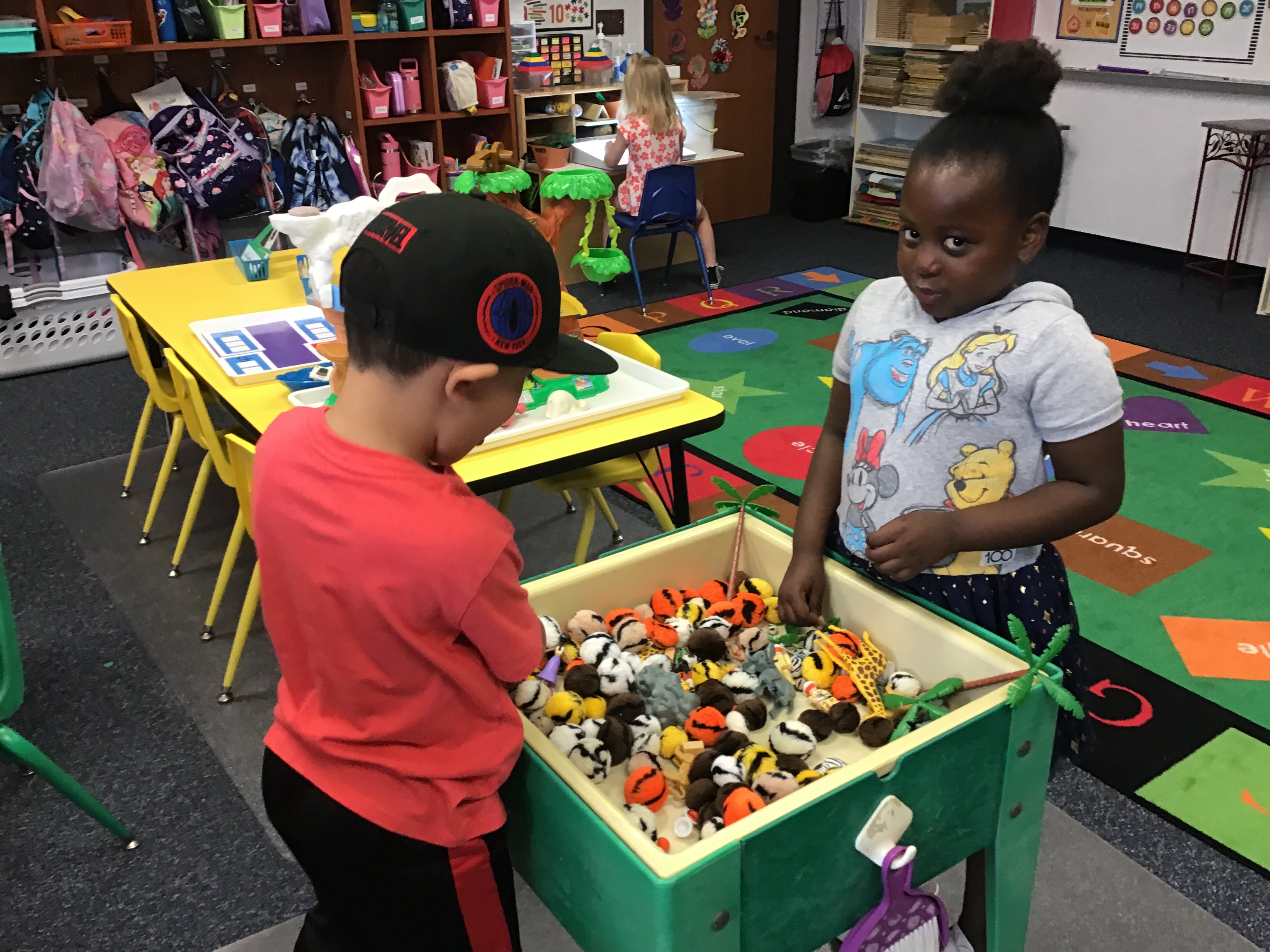 Two students playing at the sensory table filled with animal print pom poms and zoo animals.