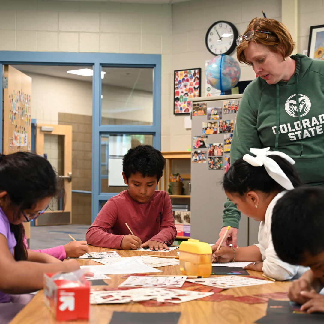 Students working together at a table on an assignment as a teacher looks onto their work.