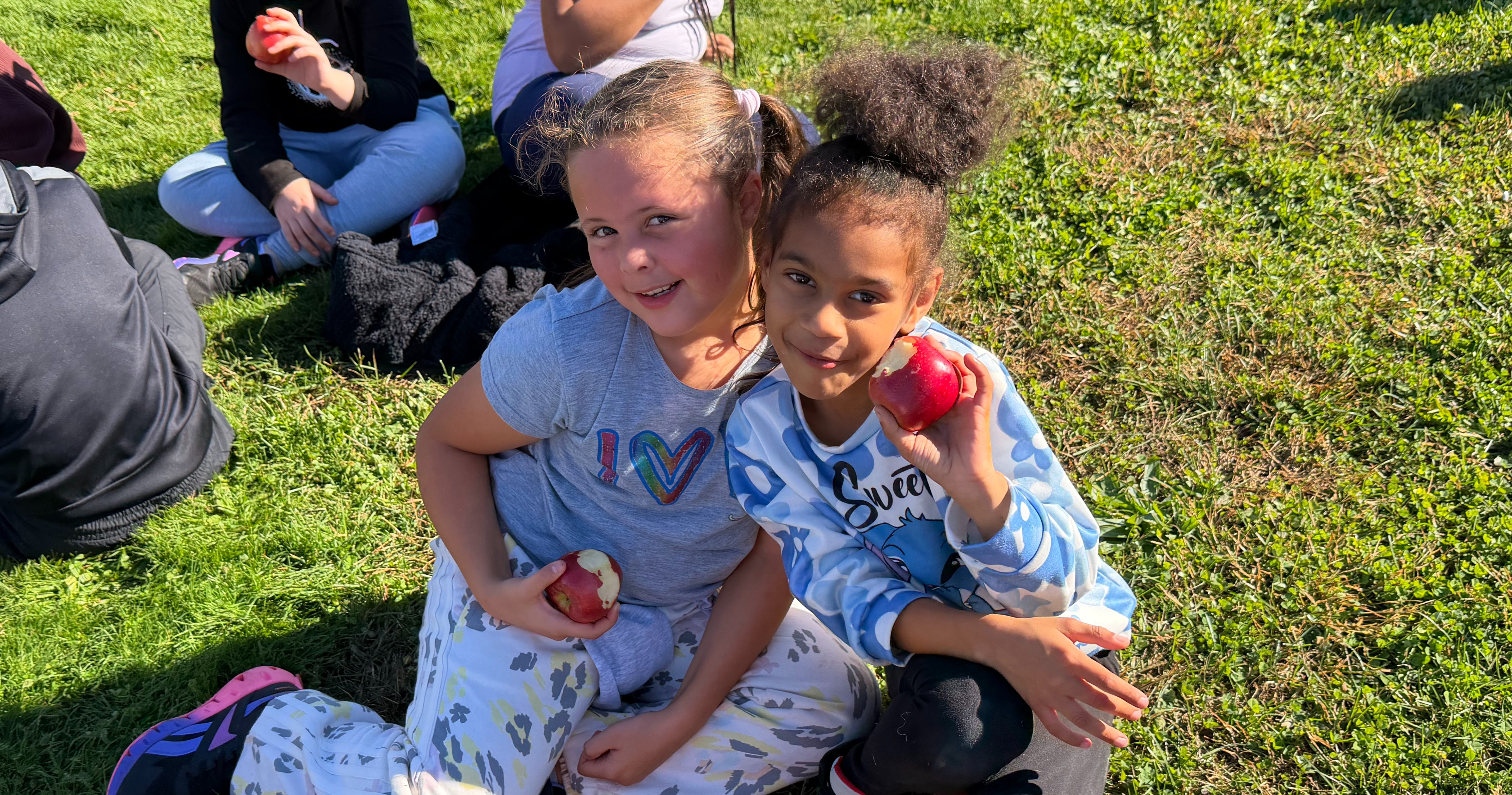 Two students sitting on the ground holding apples