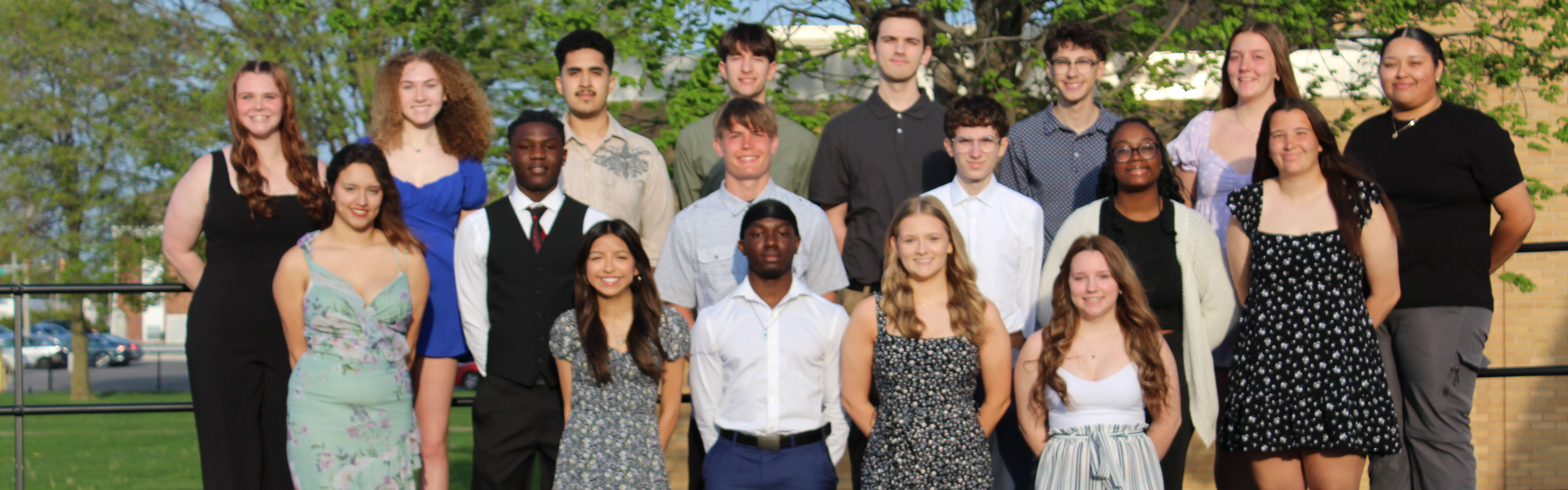 Picture of students selected for the 2025 Prom Court standing on risers in front of high school. 10 females and 8 males pictured. 2 males not pictured.