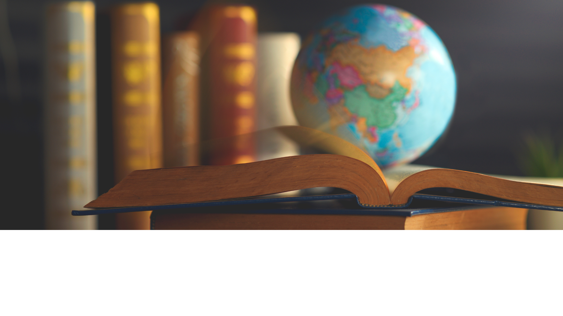 Books standing in a row and stacked with top book open and globe resting on top of it.