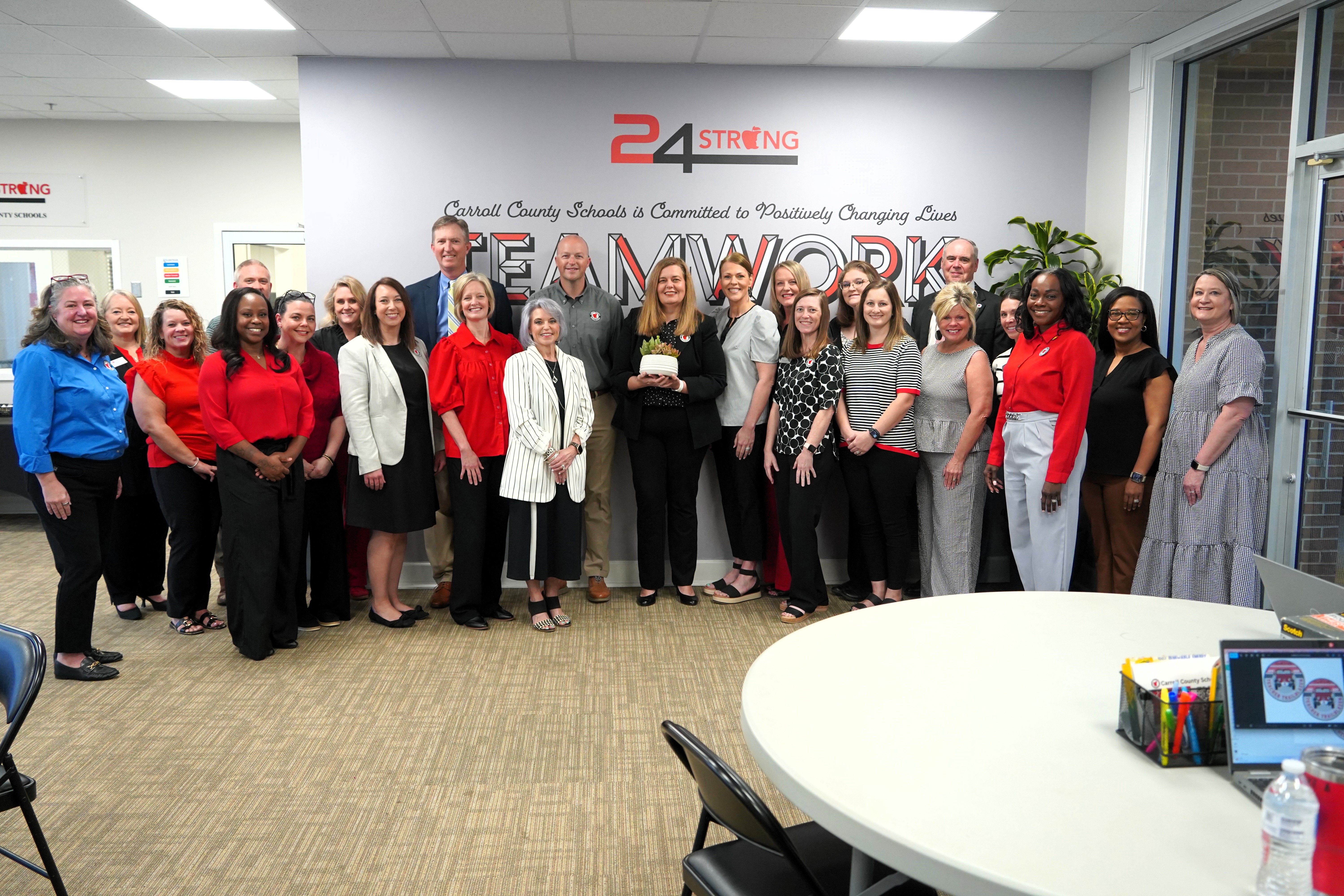 Jennifer shirley receives the April 2026 24strong award surrounded by colleagues. 