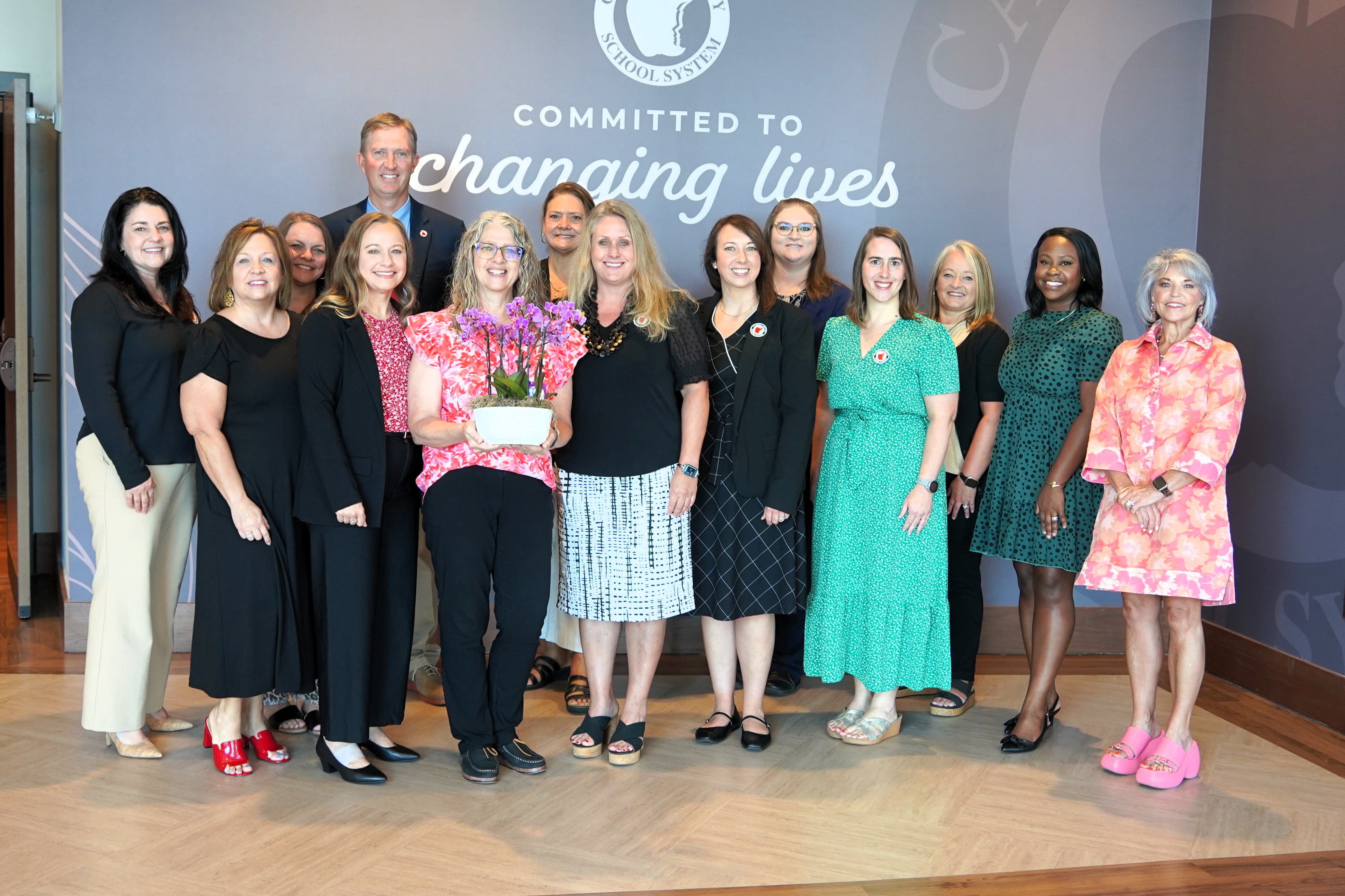 a group of carroll county employees poses with 24strong winner patty younker and a dish of orchids