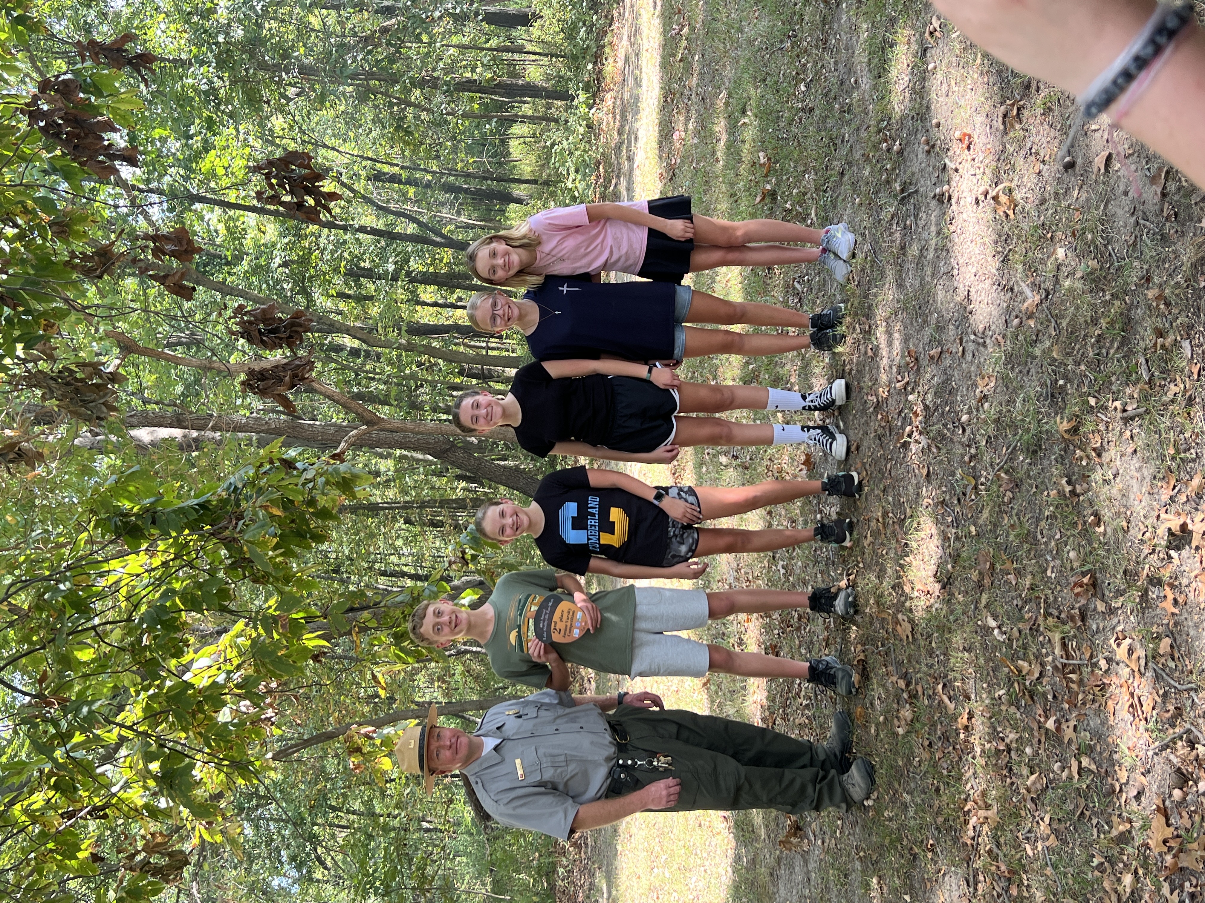 Students are standing with the park ranger. They are holding their trophy. 
