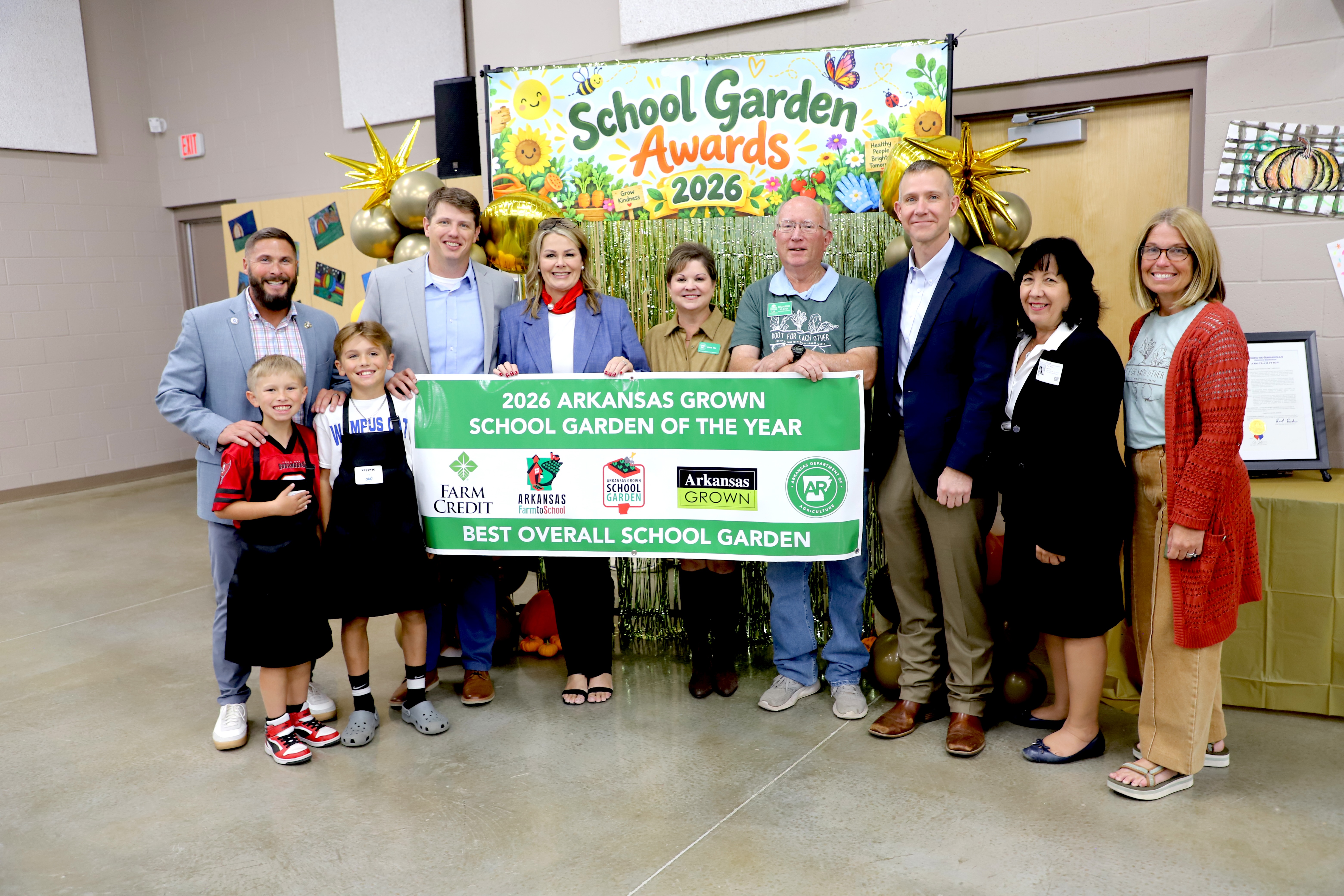A group of people stand behind a large banner and pose for a photo. Some wear aprons.