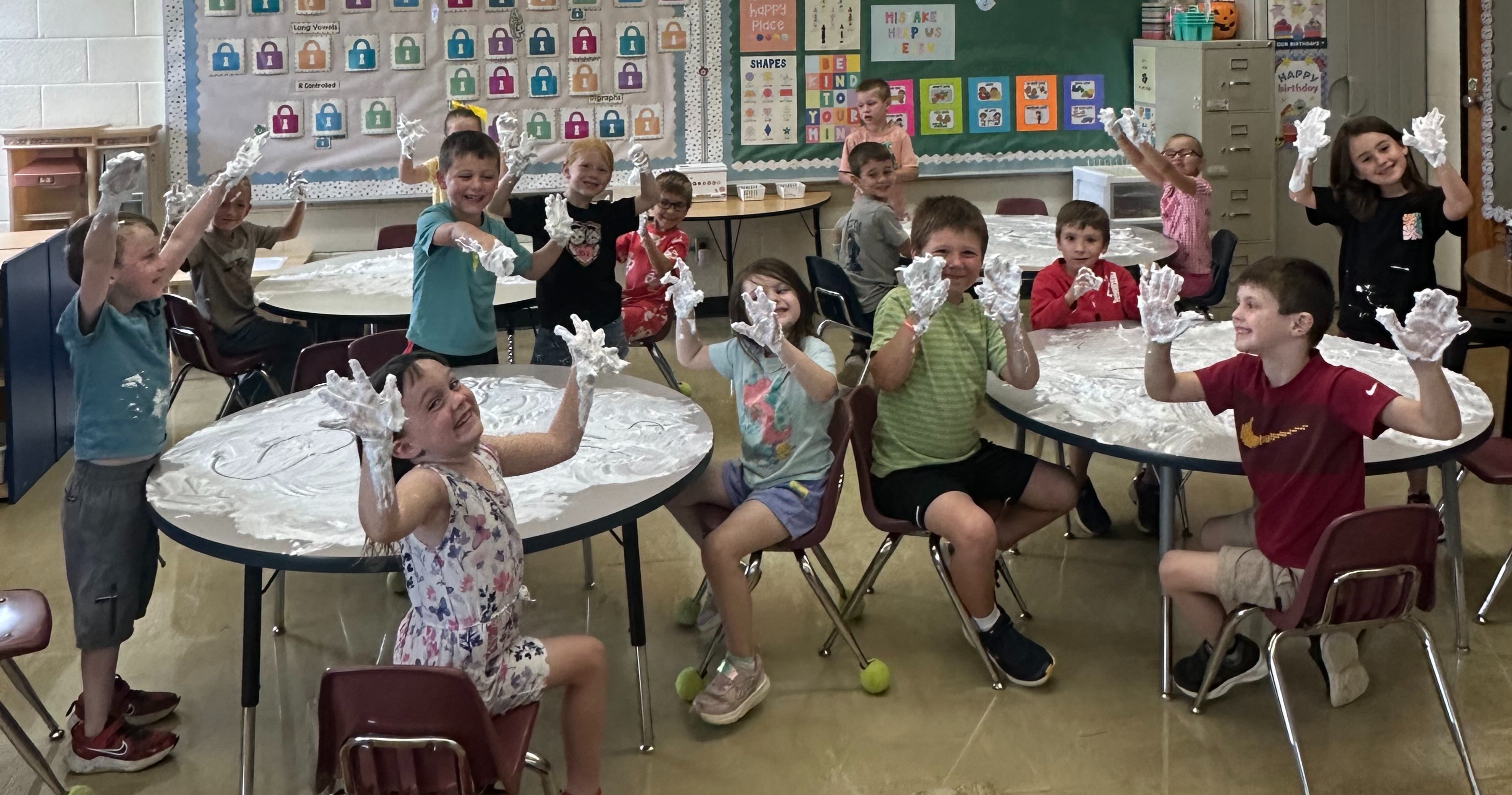 Students are sitting at tables with shaving cream on their hands.