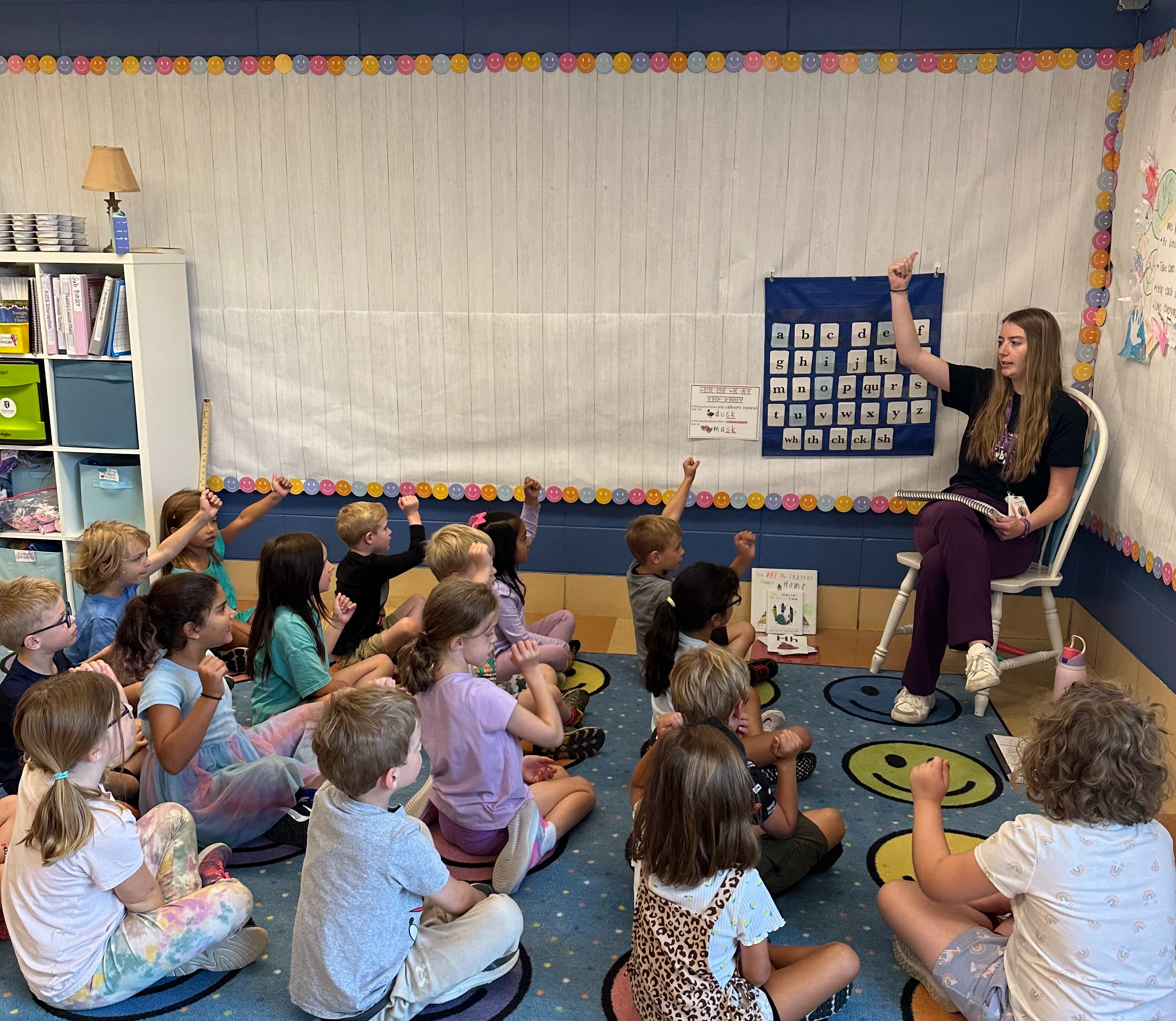 teacher sitting on chair teaching to students sitting on the floor