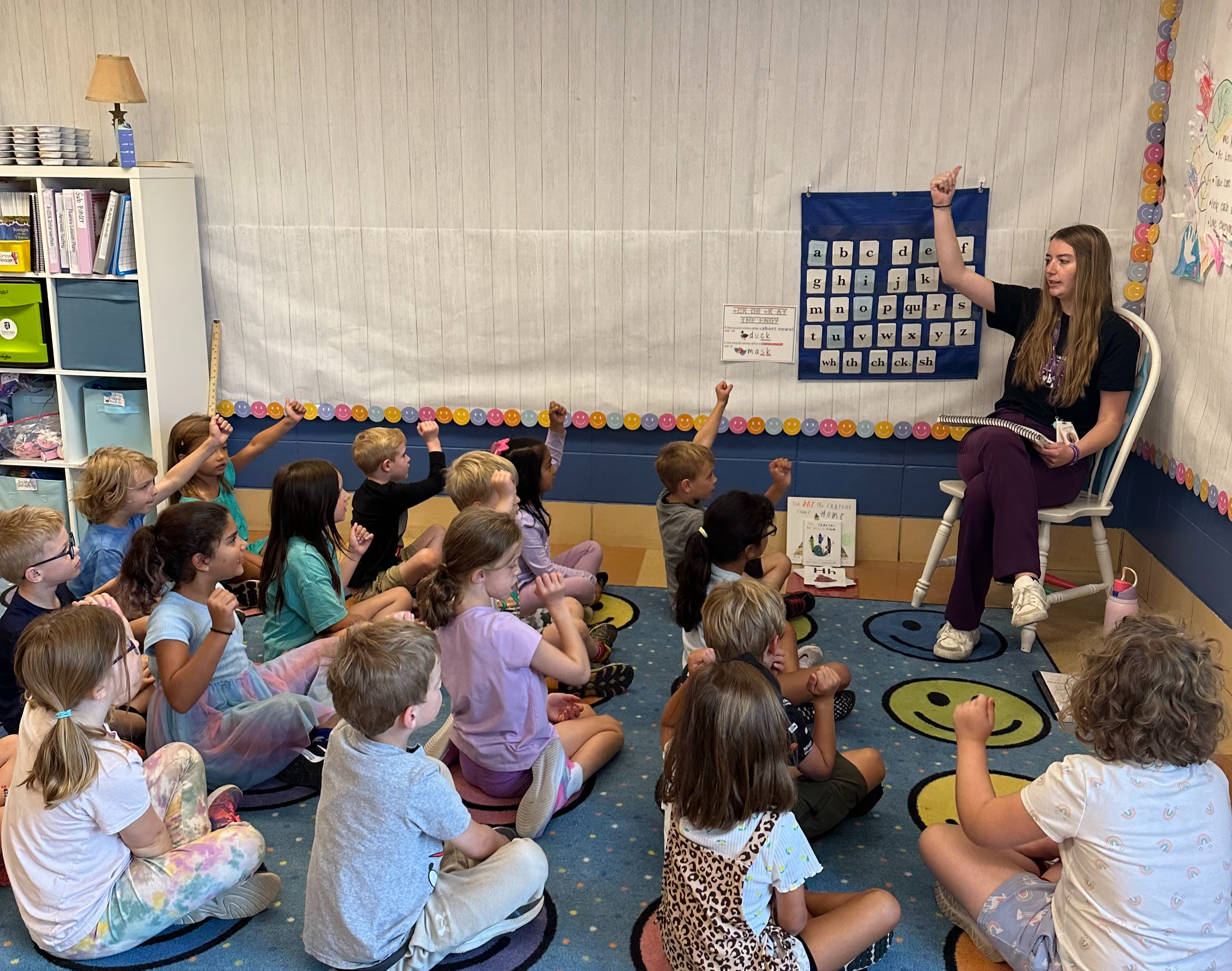 teacher sitting on chair teaching to students sitting on the floor