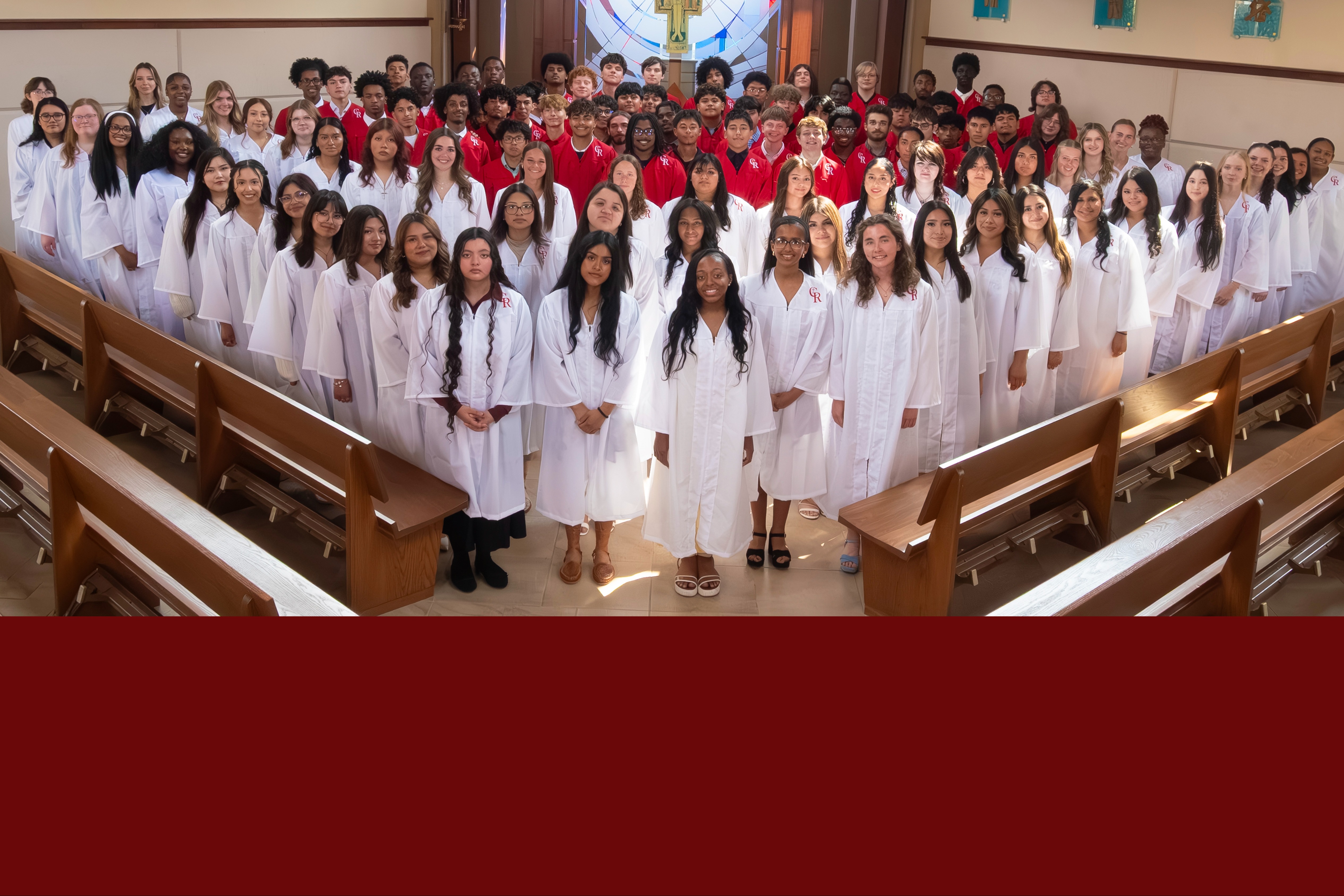Group photo of individuals in white robes and sneakers, standing in a church with wooden pews, against a backdrop of stained glass.