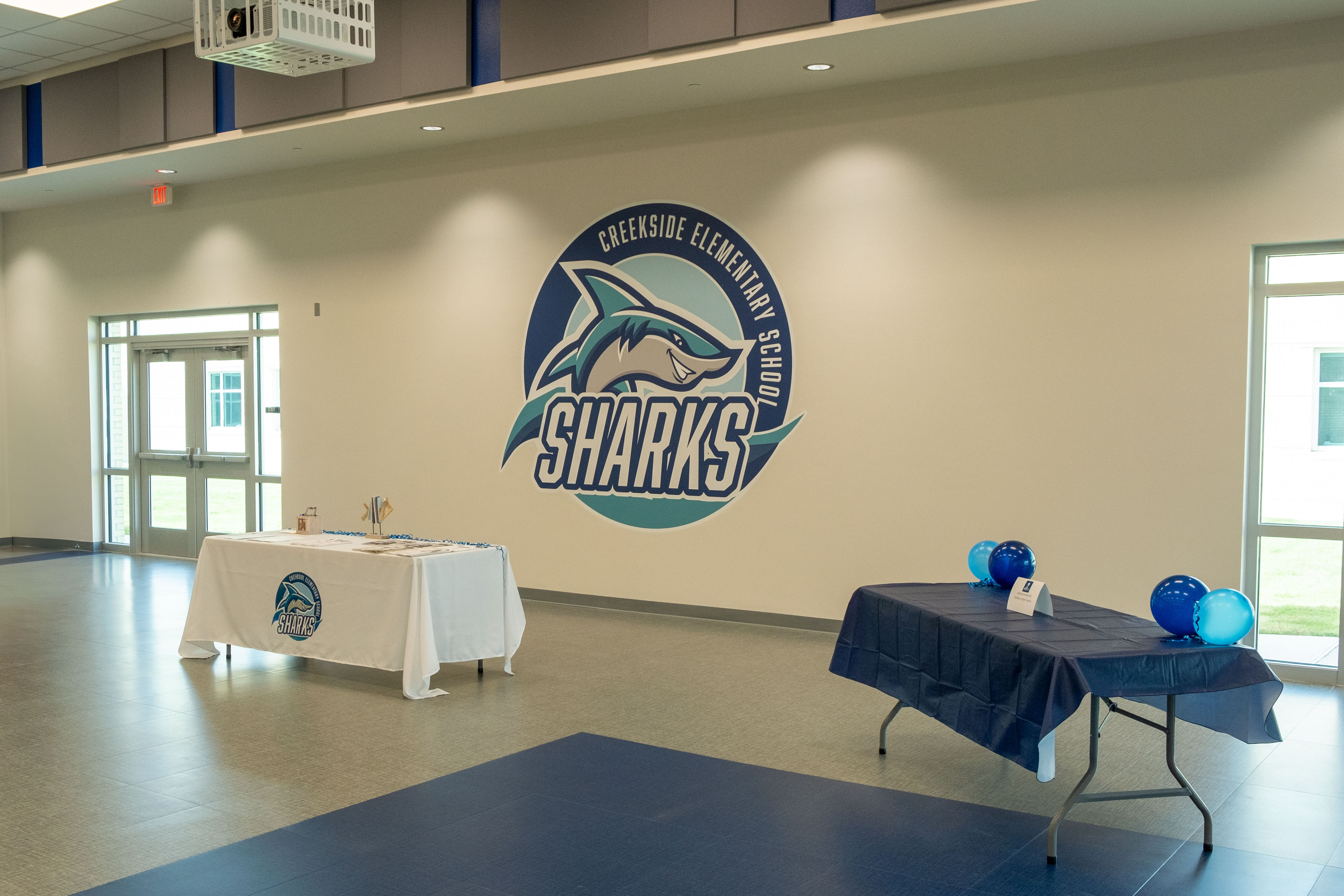 Creekside Elementary School interior featuring a large 'Sharks' logo on the wall and two tables set up for an event