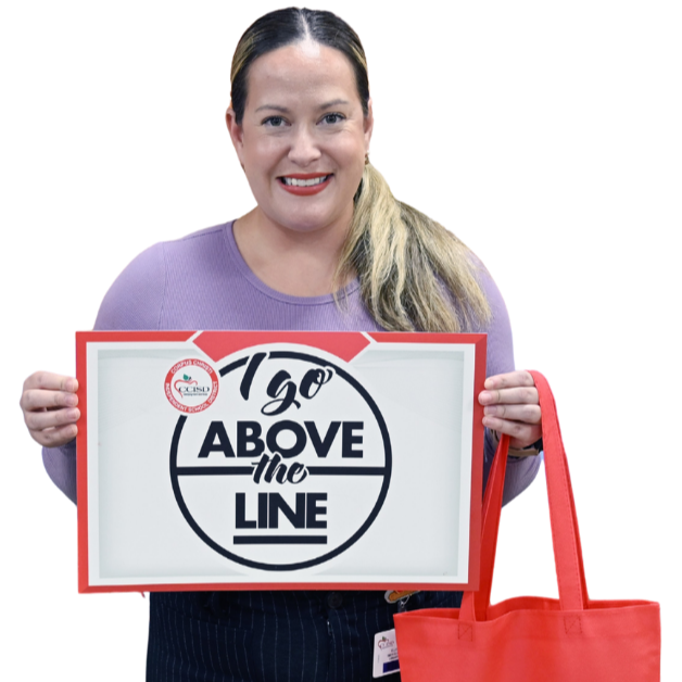 Woman in purple top holding a sign with black text reading "1go ABOVE the LINE" over black background. She holds a red bag with white logo.