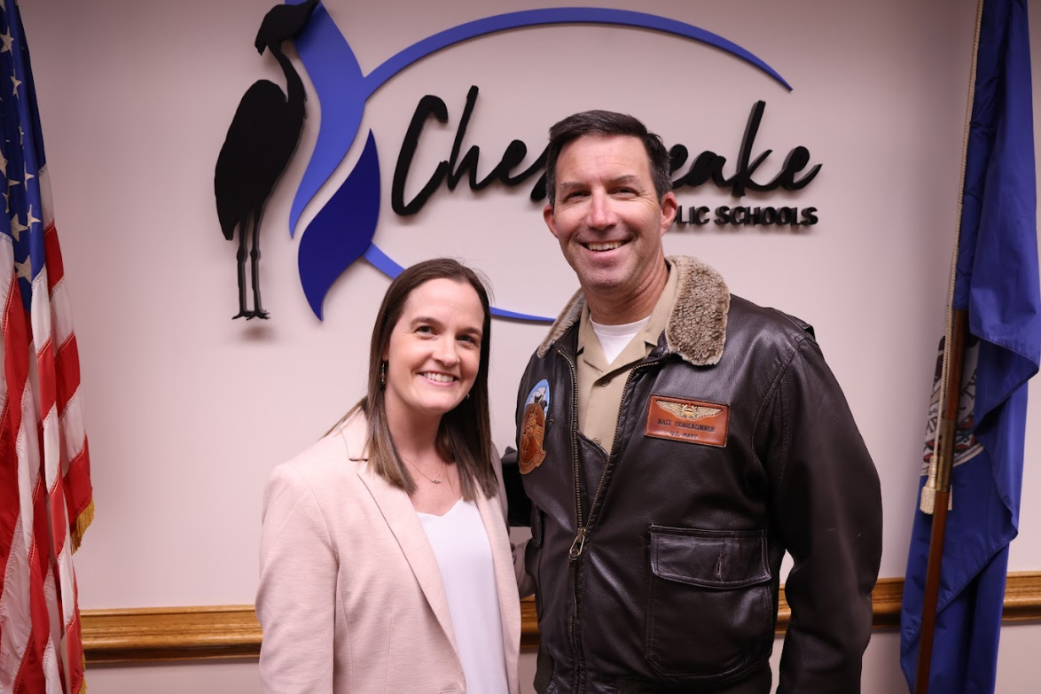 Laura and Captain Matt Frauenzimmer smiling in front of the Chesapeake Public Schools logo with the USA flag and Virginia flag surrounding them.