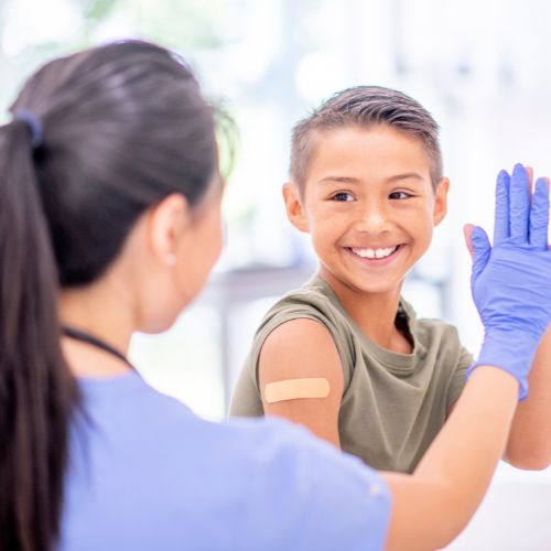 nurse high fives a child. child has a bandaid on their shoulder.