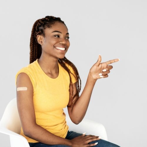 teenager with a bandaid on her arm smiles and points. 