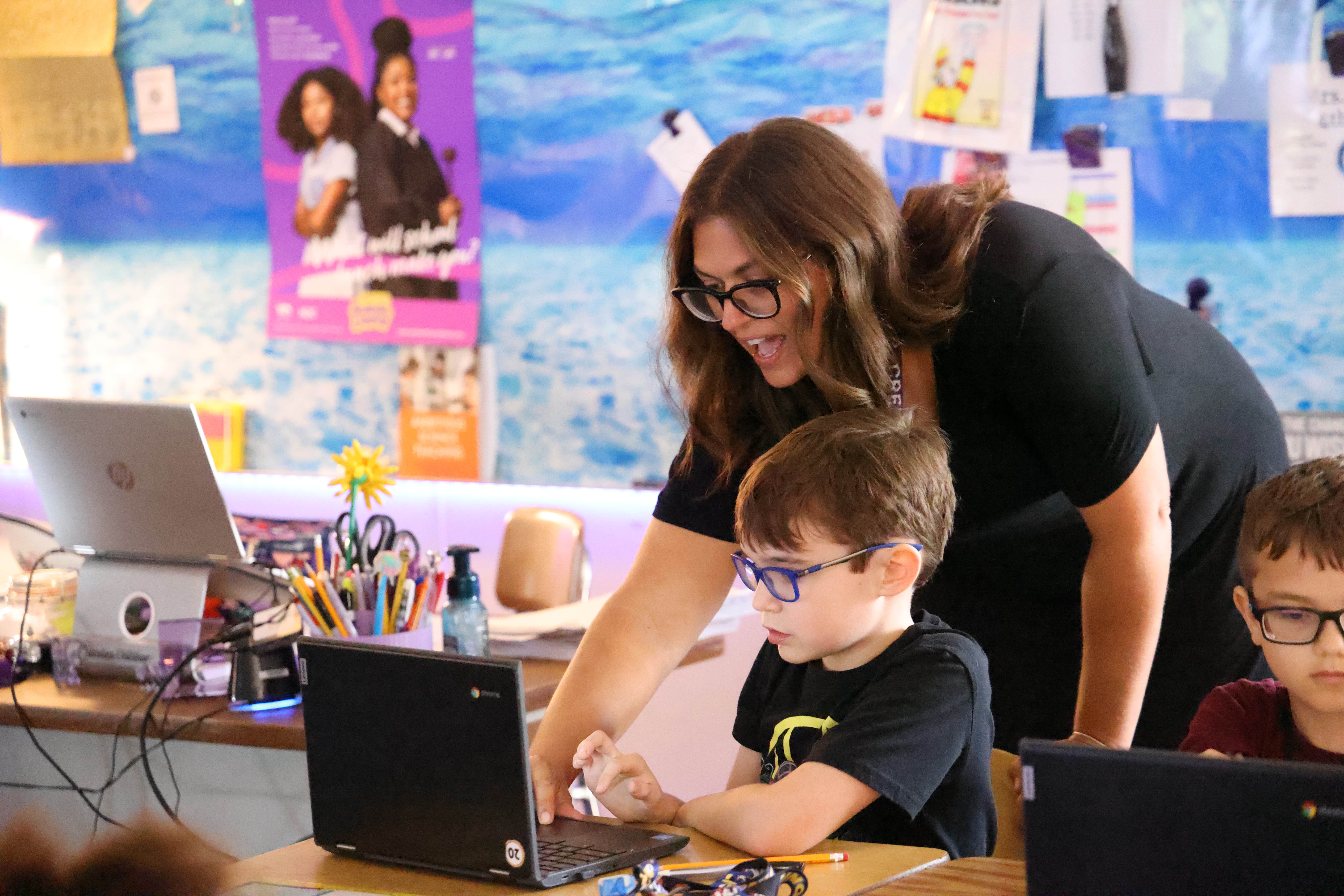 A teacher helping a student with his assignment on his laptop