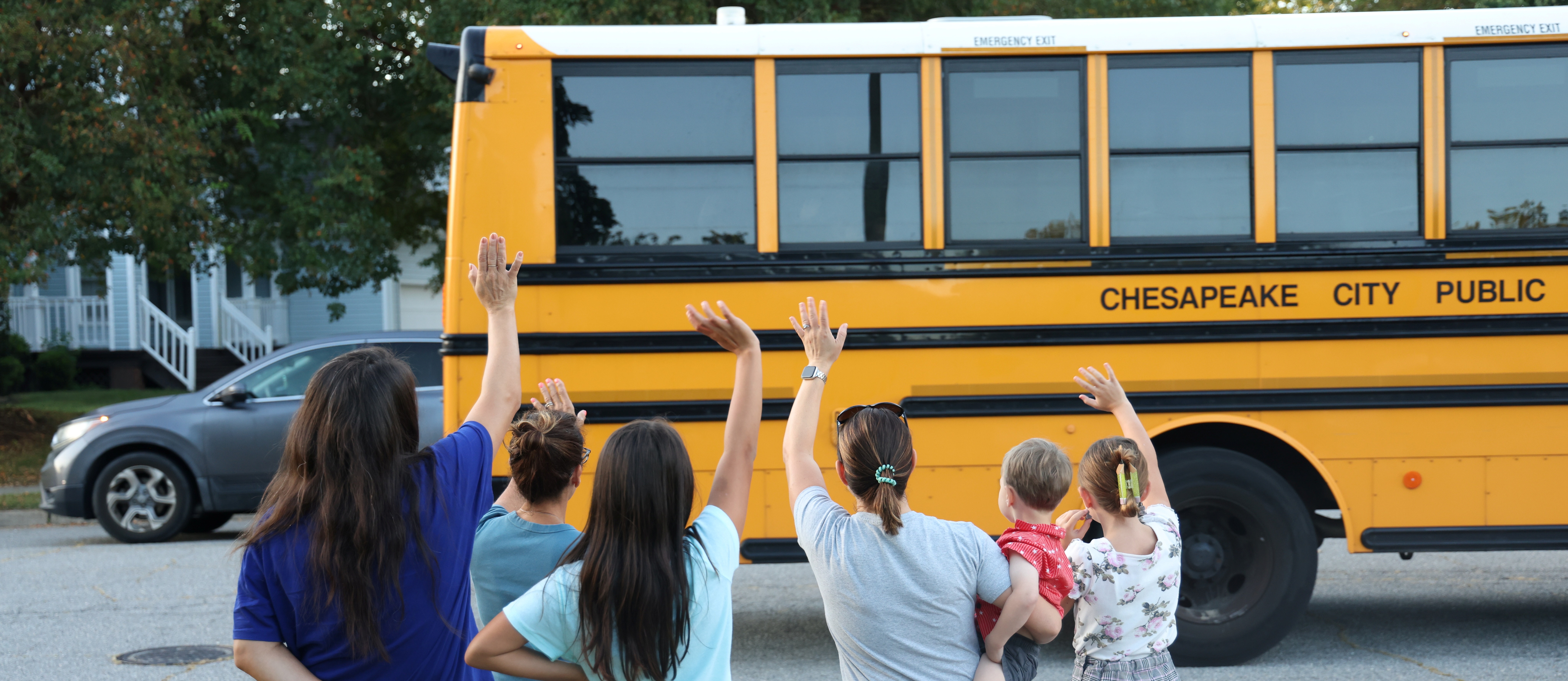 A group of neighbors waving to a departing school bus full of children