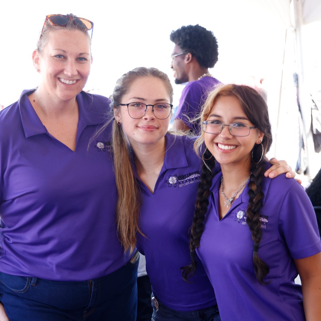 3 Members of the Science and Medicine Academy, wearing purple SMA branded polos, smile for the camera.