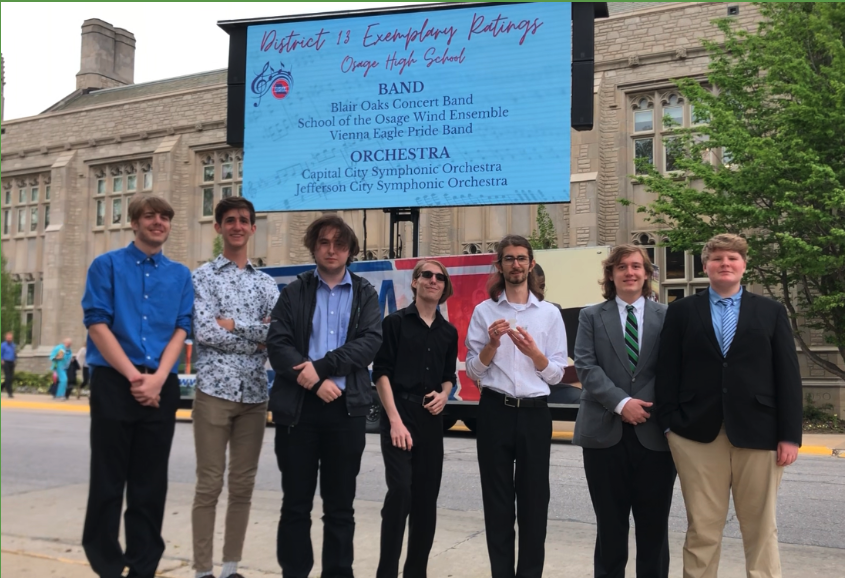 7 students in front of a digital sign for exemplary band scores