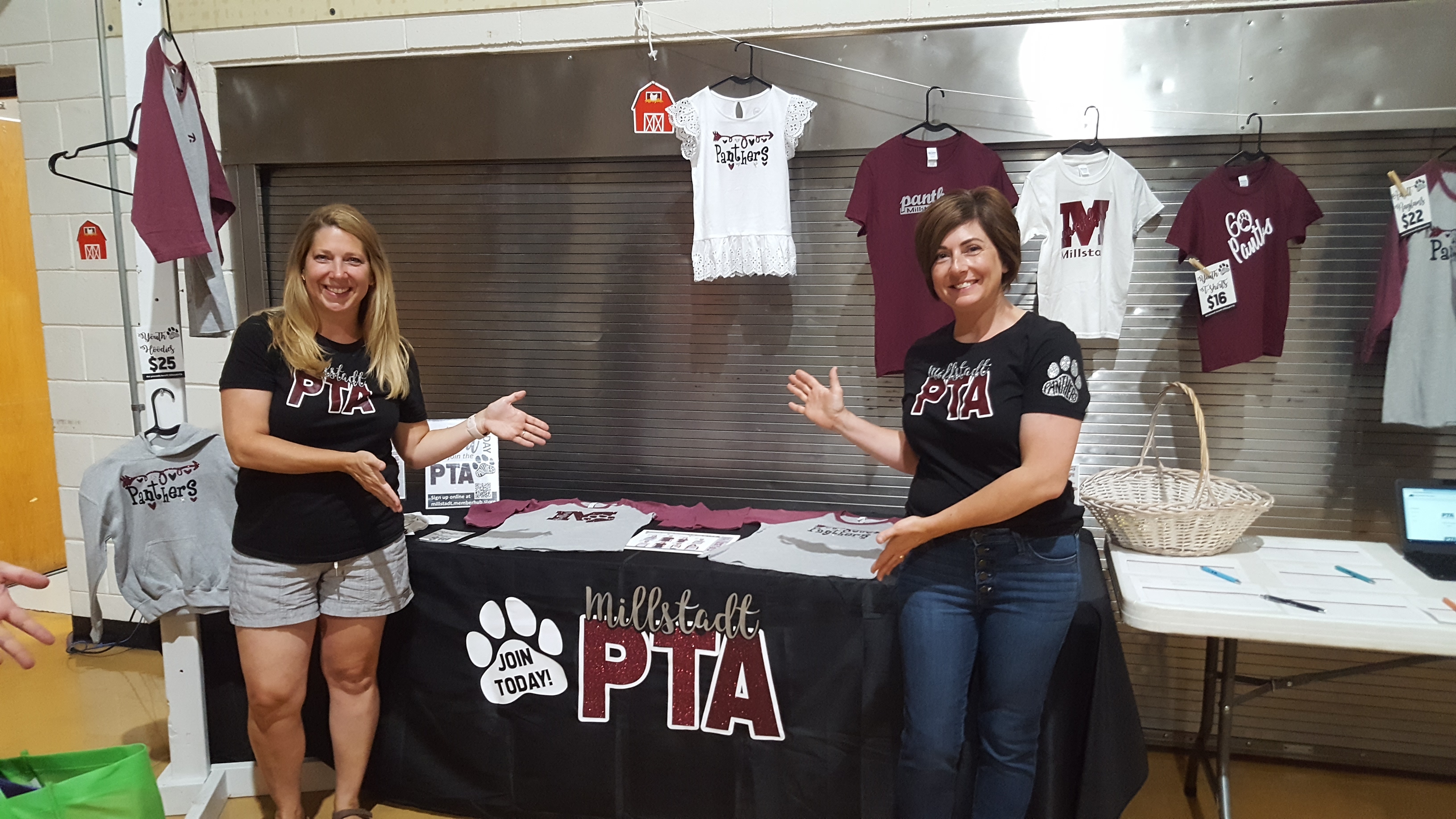 Two women, members of the pTA group, posing in front of a small standee with a small banner with their logo.