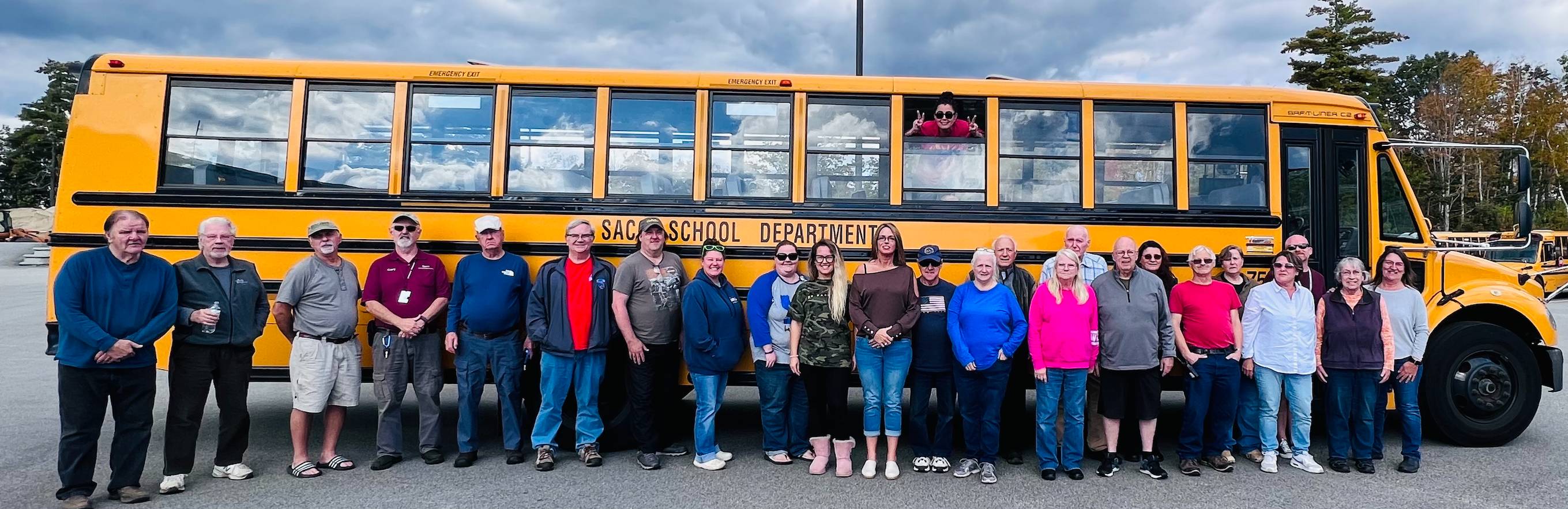 A diverse group of individuals gathered in front of a yellow school bus, smiling and engaging with one another.